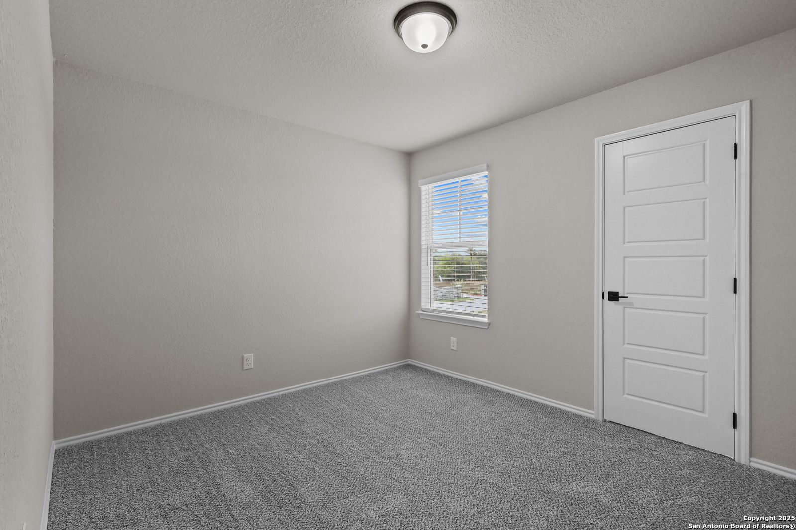 Bright secondary bedroom with light gray walls, gray carpet, white door, and window blinds in Davidson Homes The Charlotte B, San Antonio