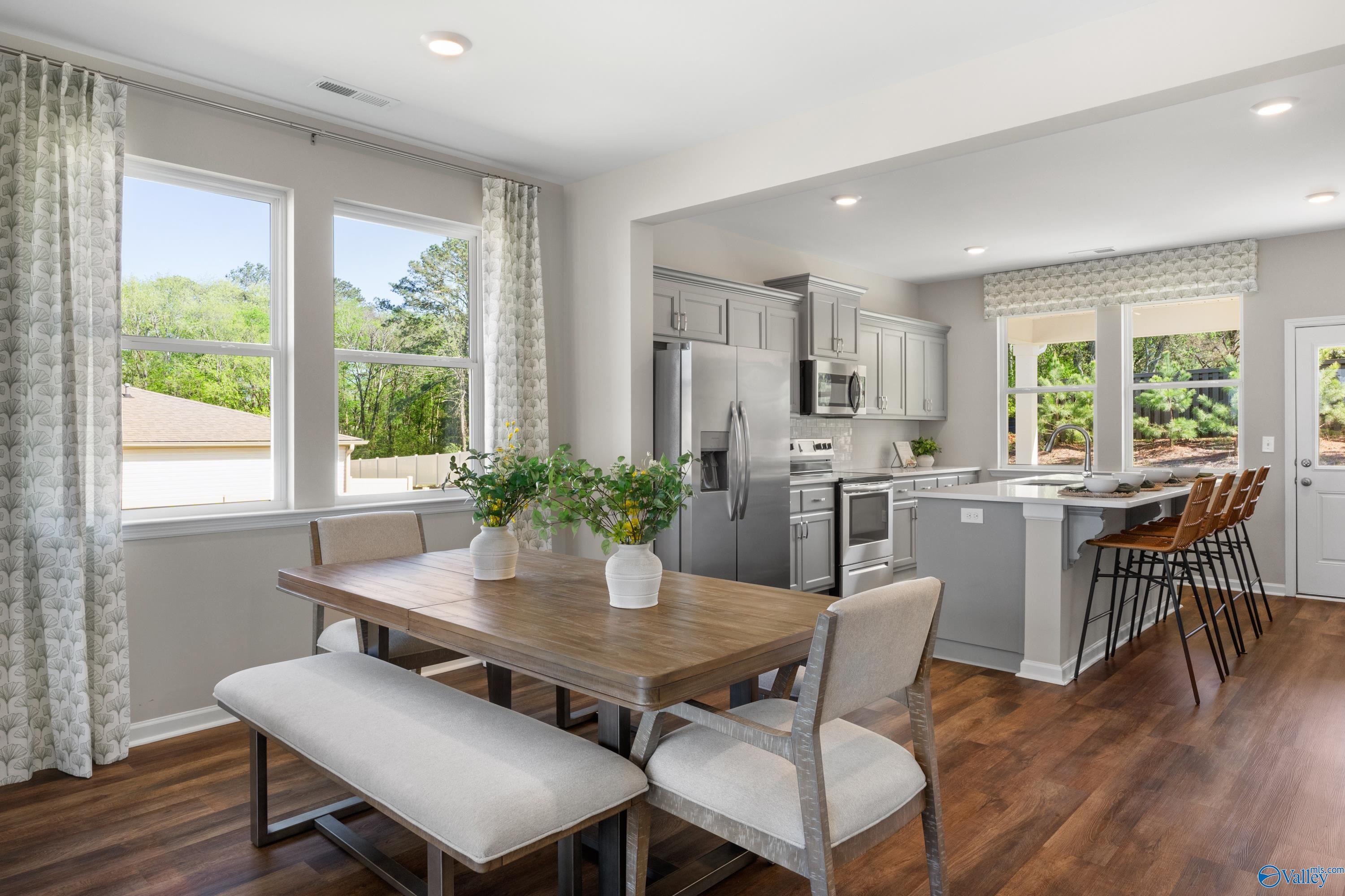 Modern open kitchen with gray cabinets, stainless appliances, large island, and dining table in The Stella floor plan, Madison Alabama