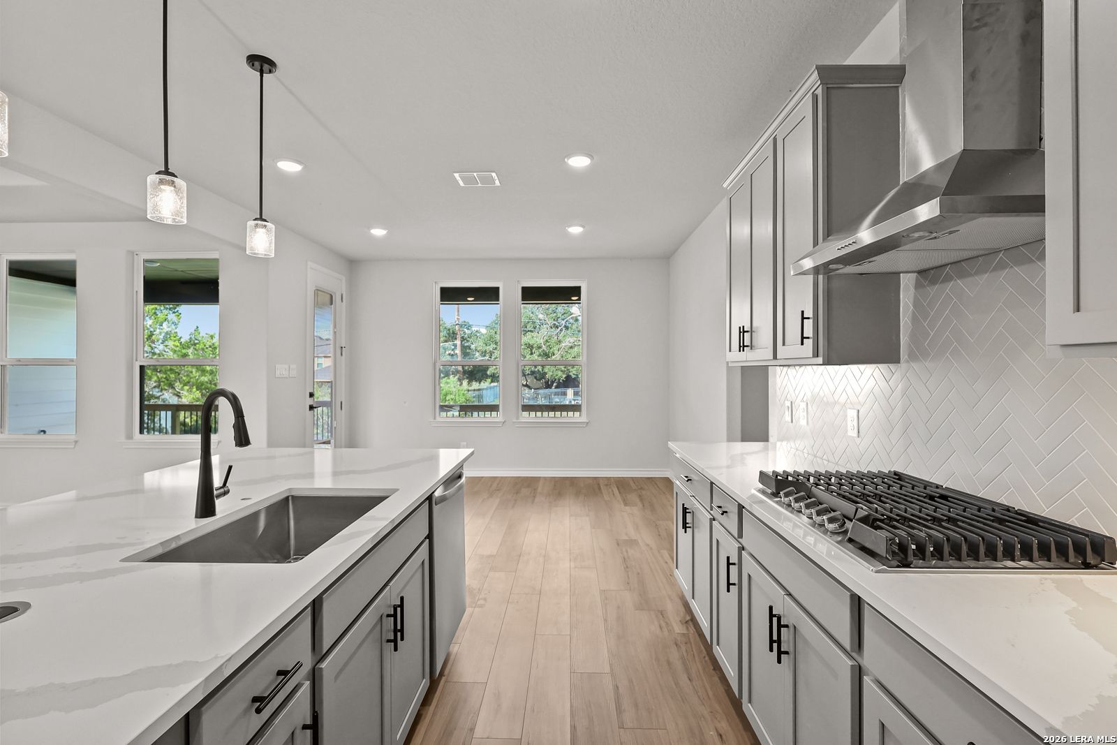 Modern kitchen with quartz island, gray shaker cabinets, herringbone backsplash in Davidson Homes Oxford F plan, Castroville TX
