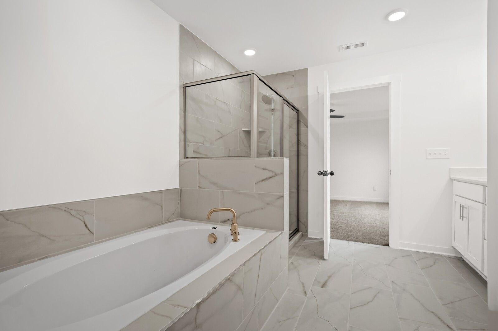 Modern primary bathroom with soaking tub, glass-enclosed shower, and gold fixtures in Davidson Homes' Logan C floor plan.