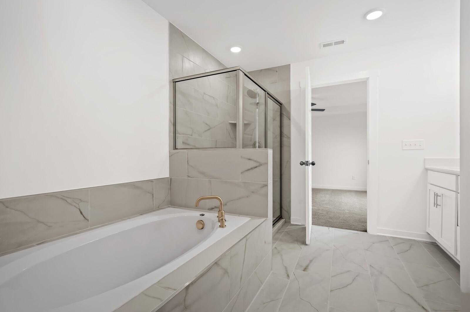 Modern primary bathroom with soaking tub, glass-enclosed shower, and gold fixtures in Davidson Homes' Logan C floor plan.