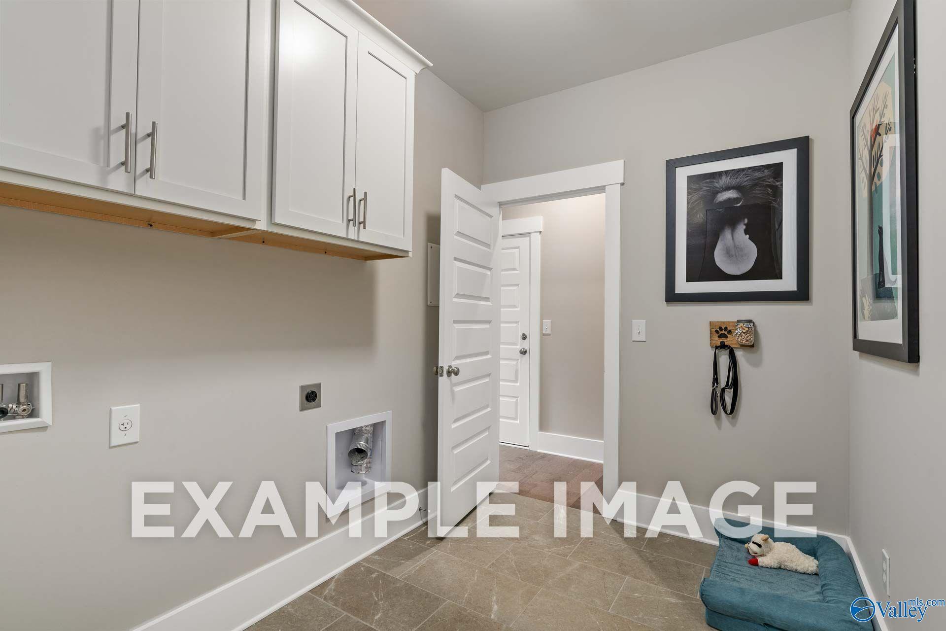 Mudroom laundry room with white cabinets, tile flooring, and pet bed in Davidson Homes The Harrison floor plan, Hartselle, Alabama