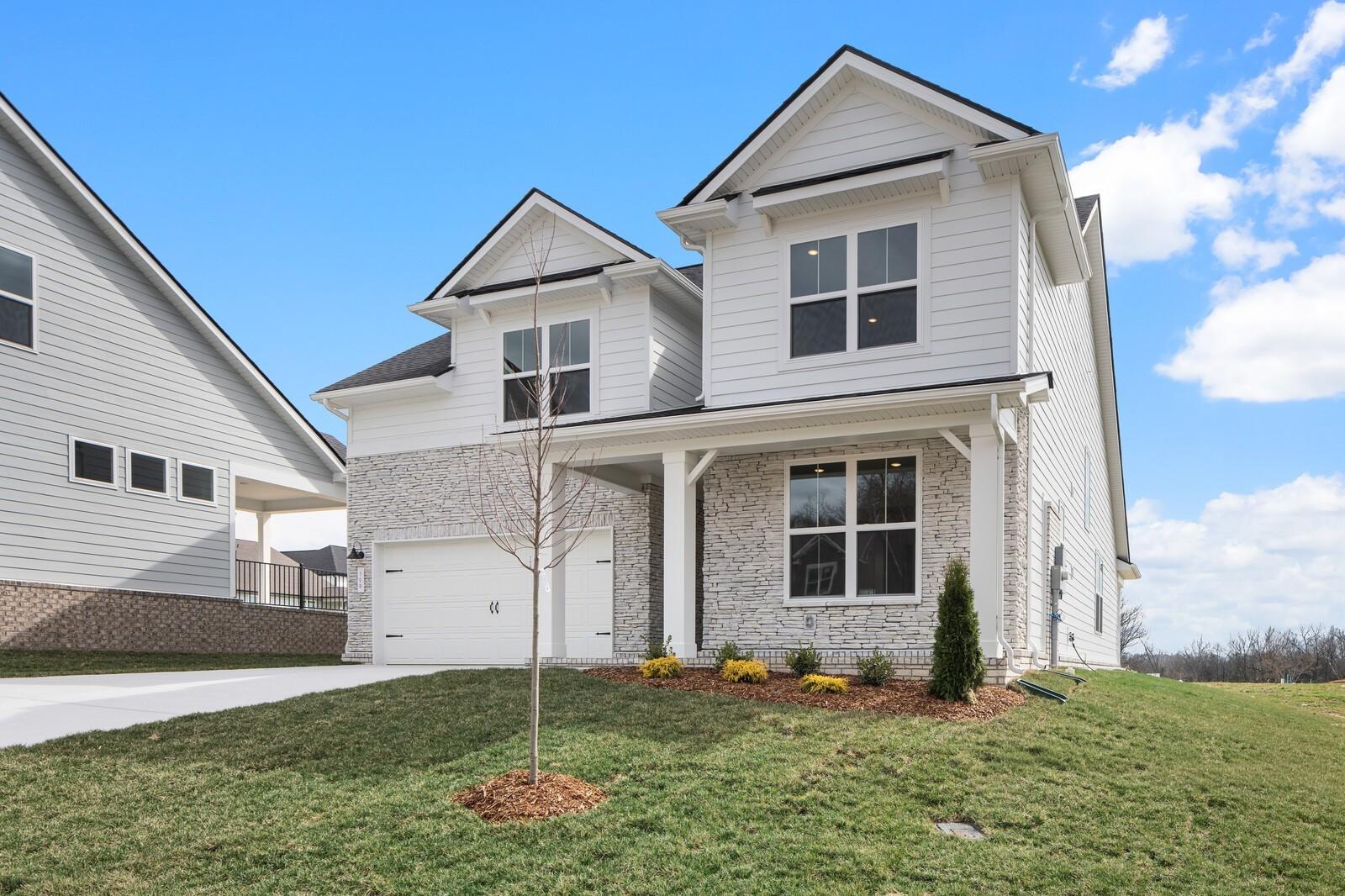 Two-story Ridgeport home by Davidson Homes with white brick exterior, covered porch, large windows, and 2-car garage in Woods Crossing, Gallatin, Tennessee