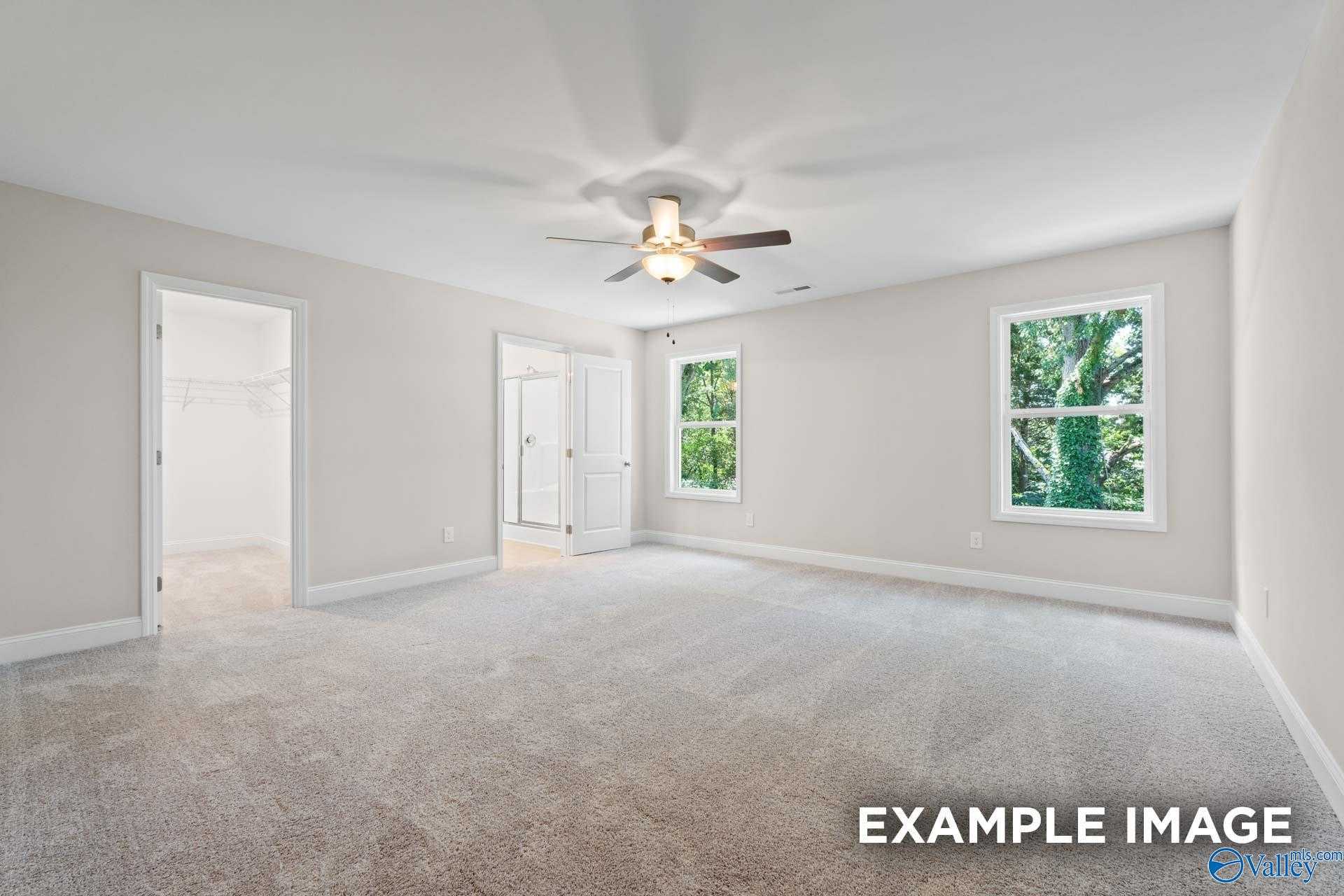 Spacious empty bedroom with beige walls, carpet floor, ceiling fan, and windows to greenery in Davidson Homes The Camden C, Huntsville
