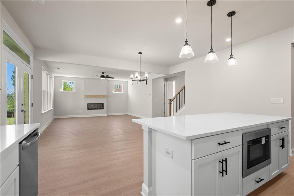 Open kitchen with white quartz island, microwave drawer, dishwasher, fireplace, and backyard view in Hickory E home, Buford, Georgia