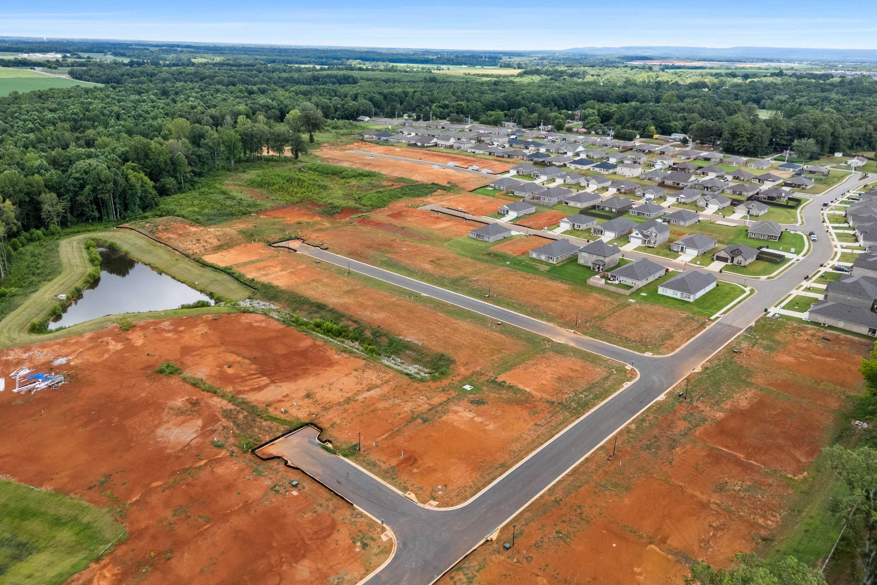 Aerial view of Wood Trail neighborhood in Toney Alabama with new homes, red dirt lots, pond and wooded fields
