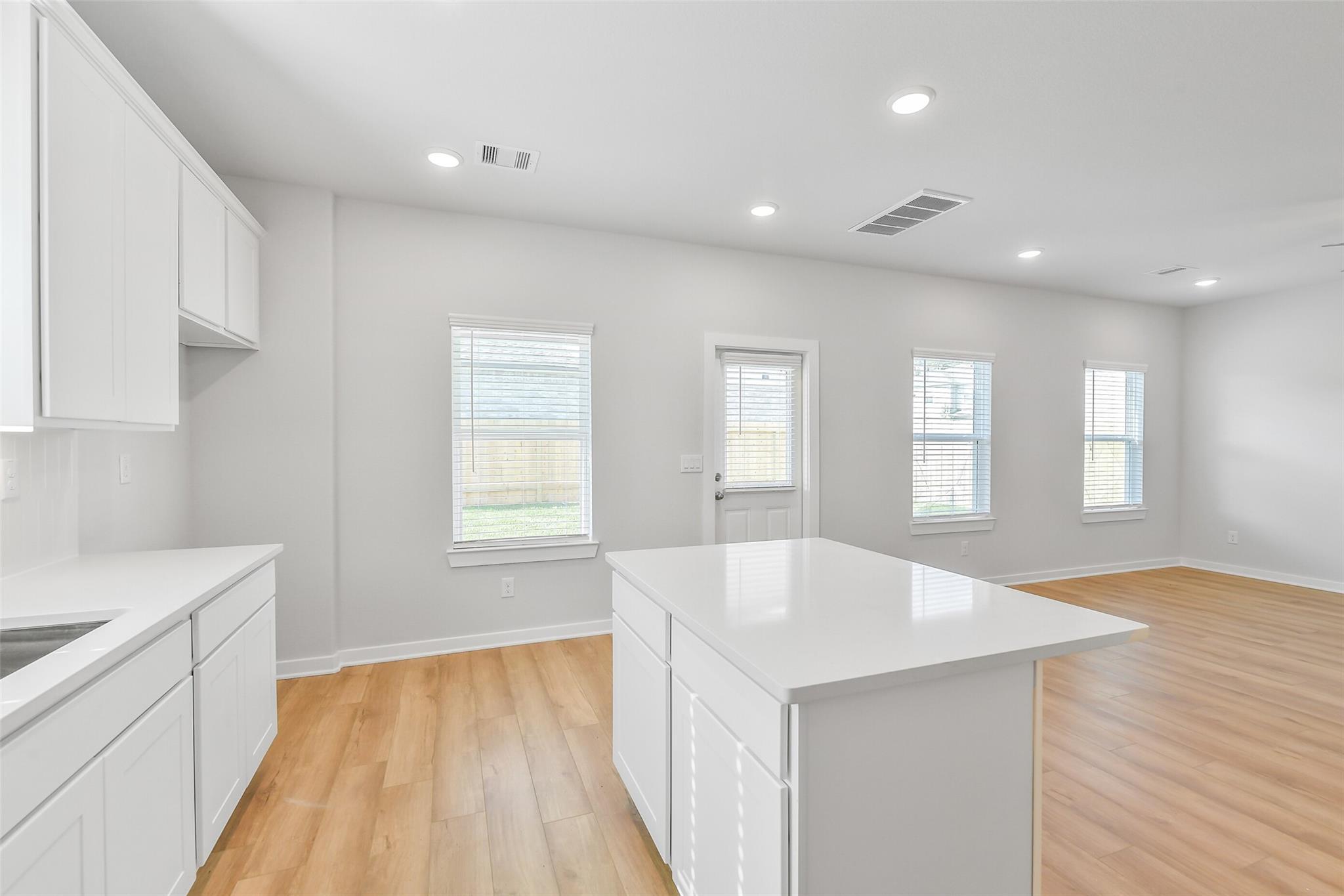 Modern white kitchen island with quartz counters, hardwood floors, and large windows in Davidson Homes The Trinity F, Magnolia, Texas