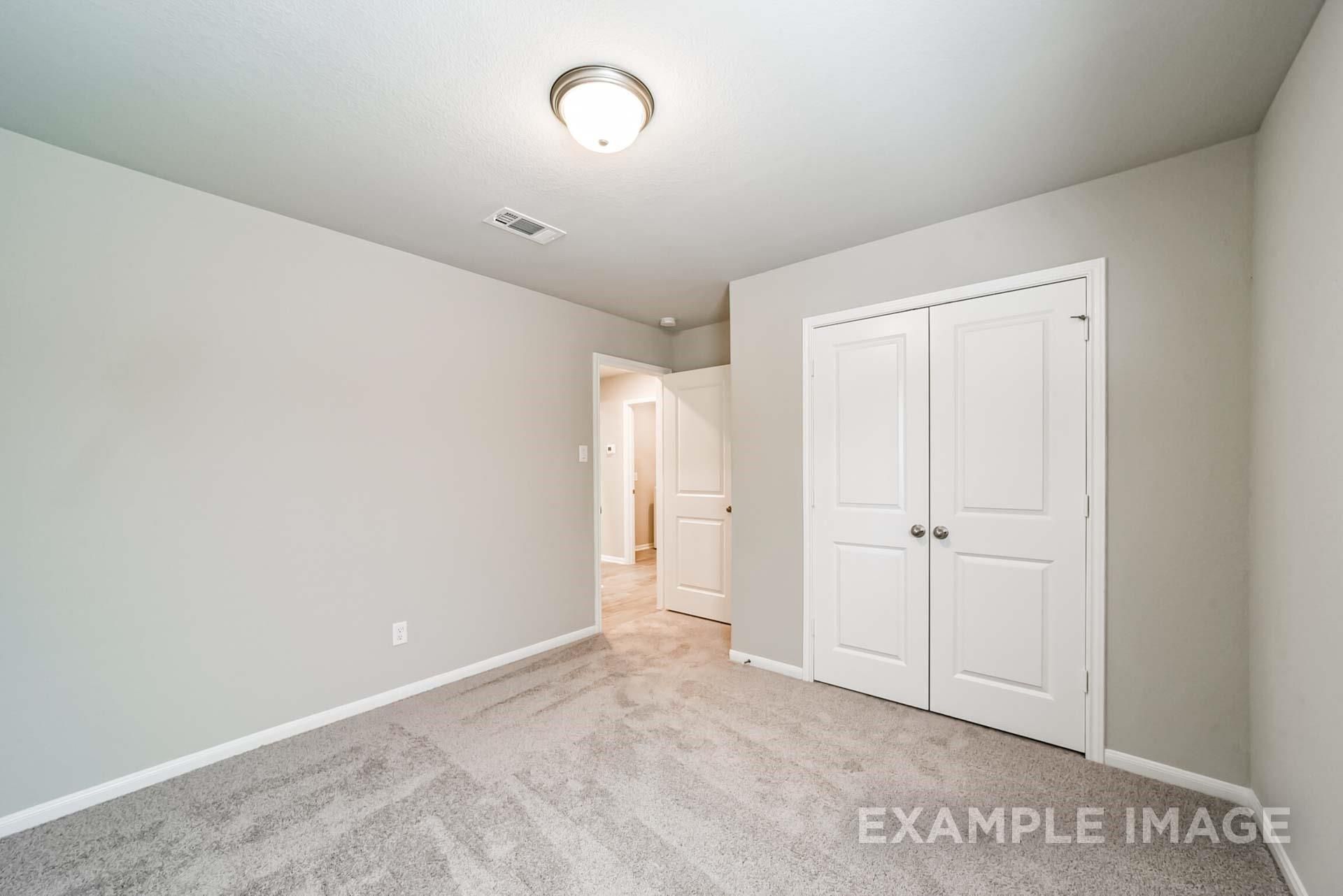 Spacious secondary bedroom with neutral carpet and double-door closet in The Riviera A floor plan at Emberly, Beasley, TX.