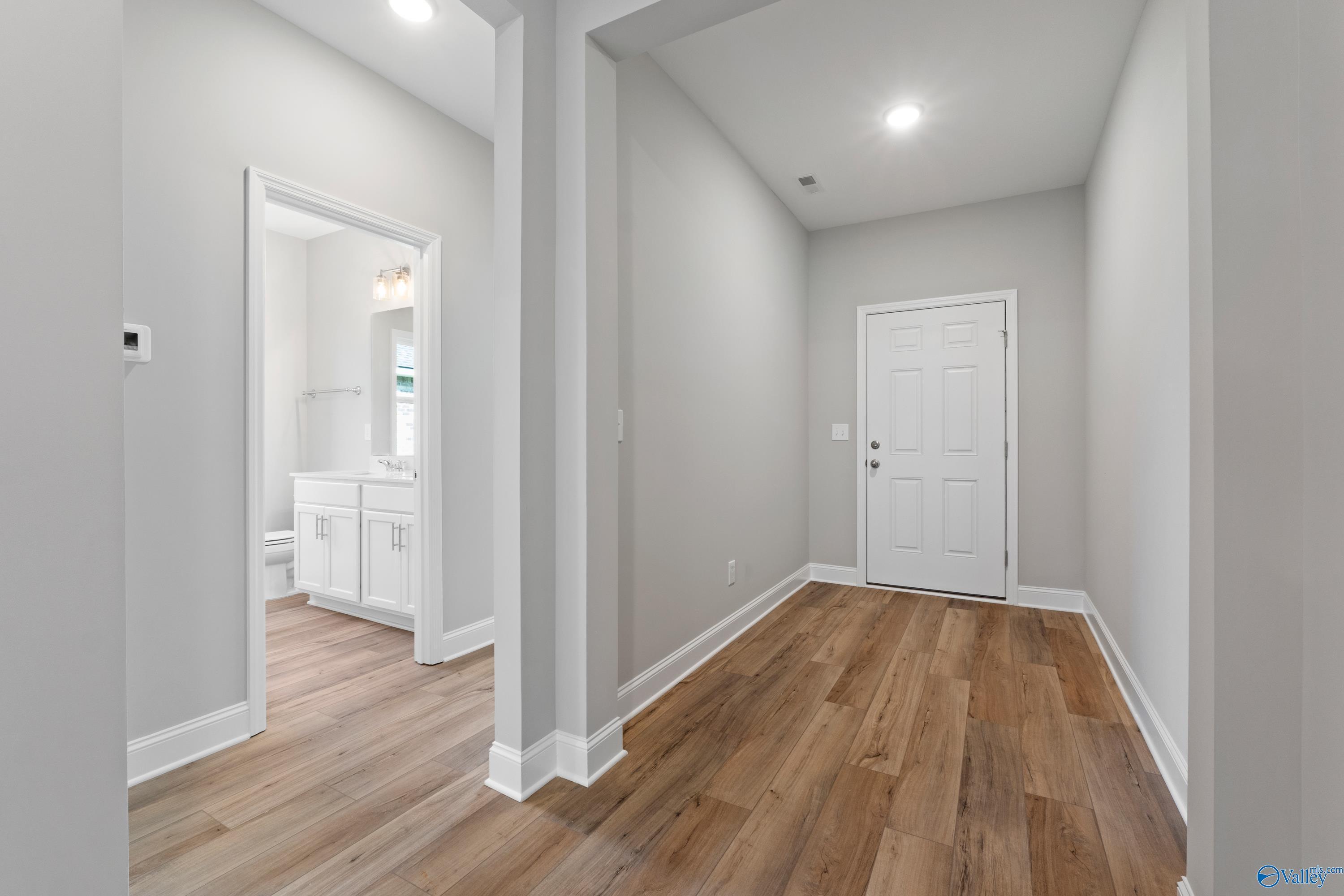 Bright hallway with open bathroom door, white vanity, and hardwood floors in Davidson Homes The Everett B, Toney, Alabama