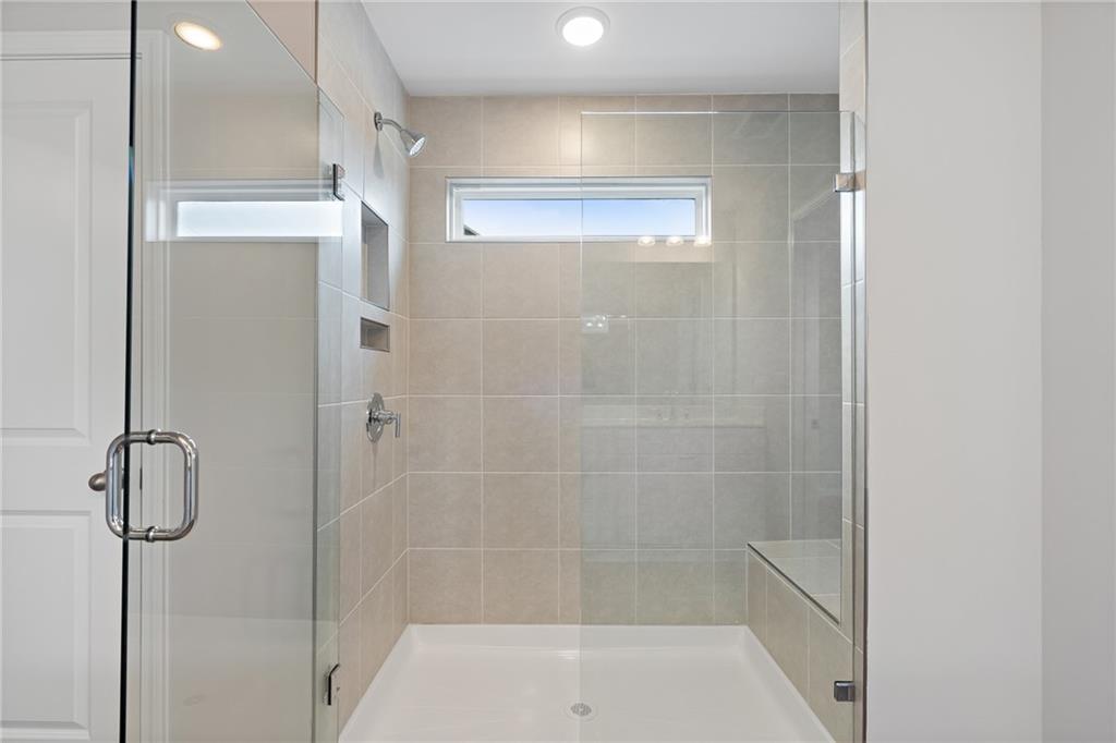 Modern frameless glass shower with beige subway tiles, bench seat, and niche in master bath of The Hickory A, Davidson Homes, Winder, GA