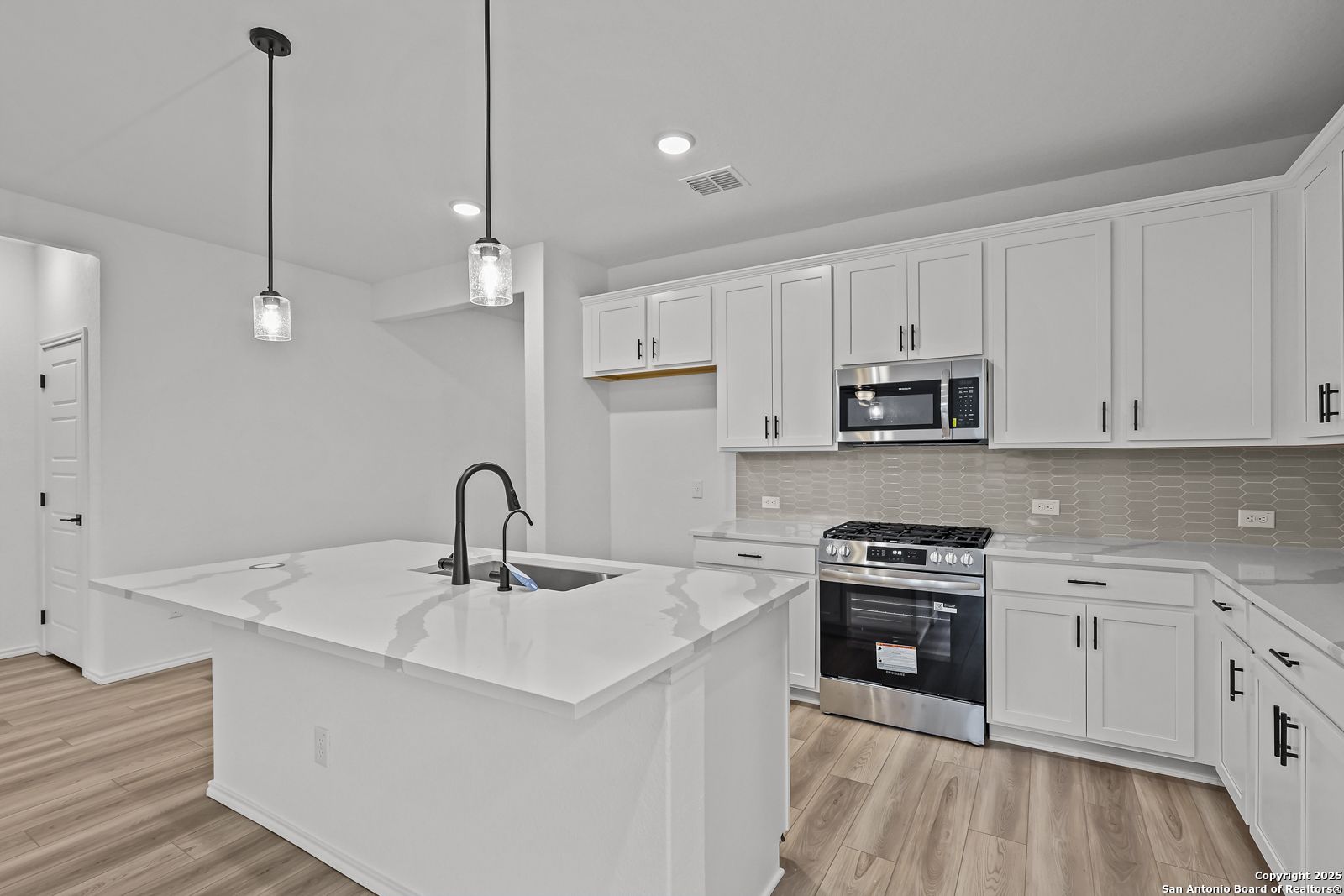 Modern kitchen featuring white shaker cabinets, quartz island sink, stainless gas range in The Daphne J by Davidson Homes, Converse TX