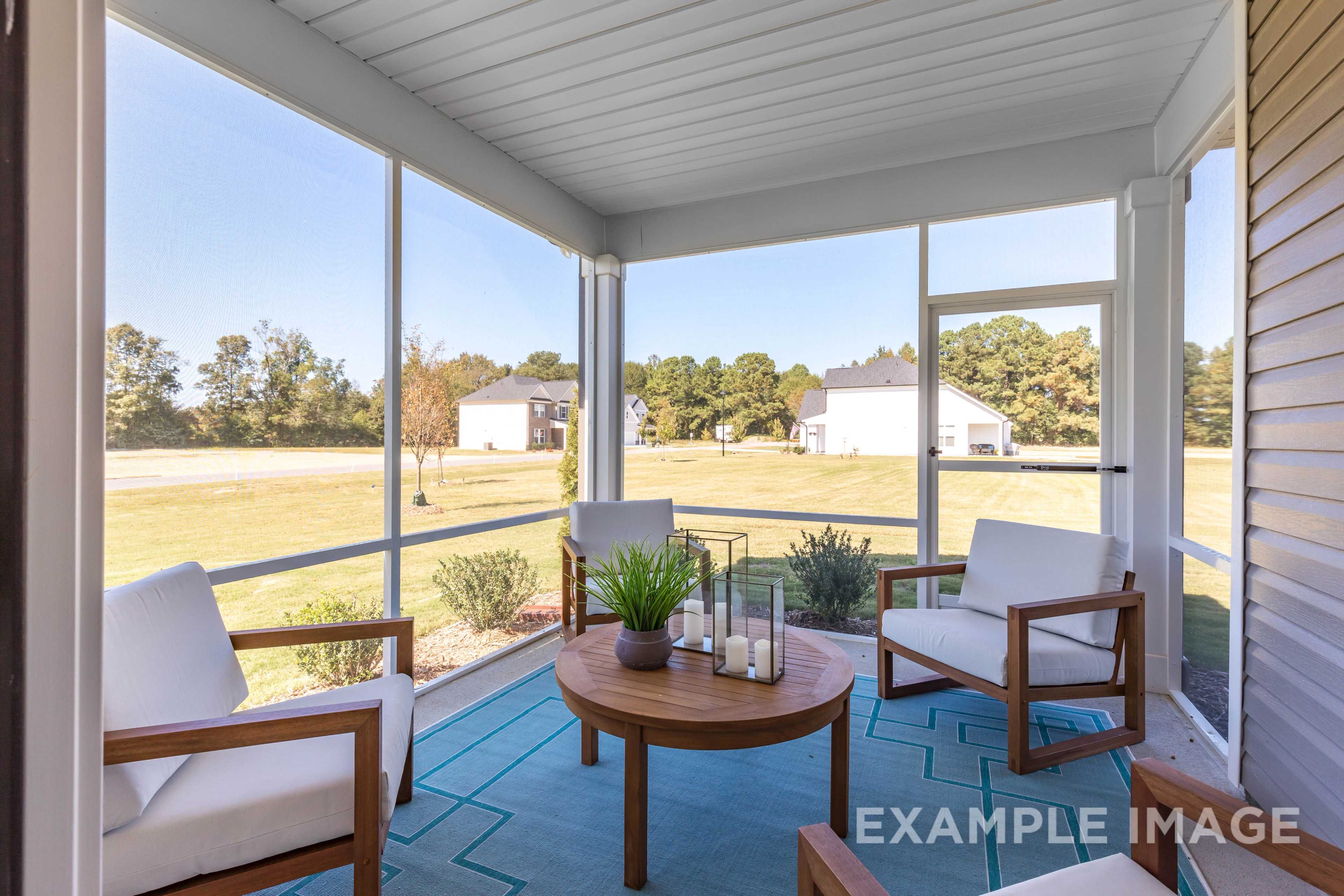 Spacious screened porch in The Ash C home with wicker chairs, round table, candles, plants, and grassy backyard view