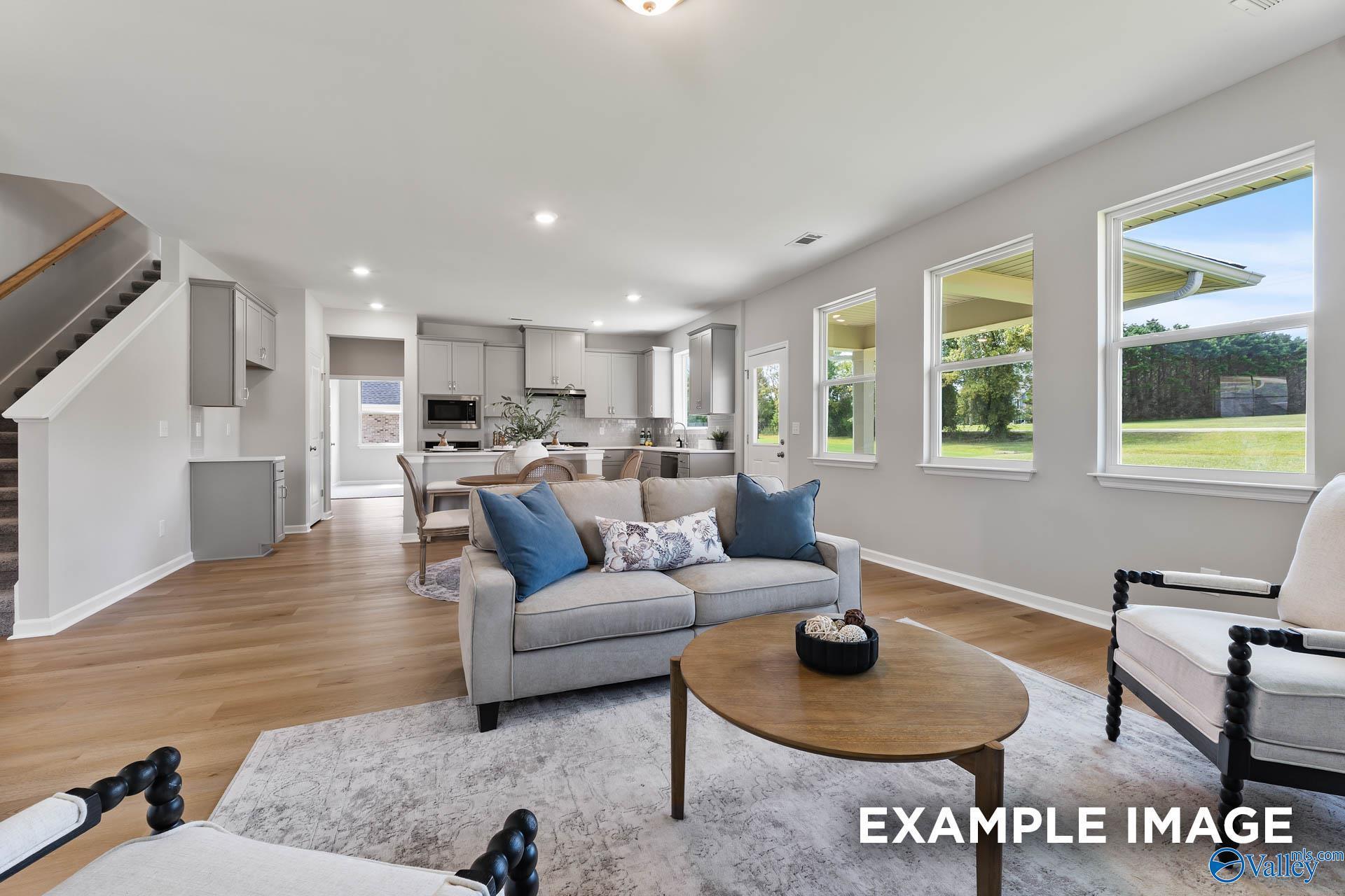 Bright open-concept living room with gray sofa, coffee table, and kitchen overlook in Davidson Homes The Charm, Huntsville