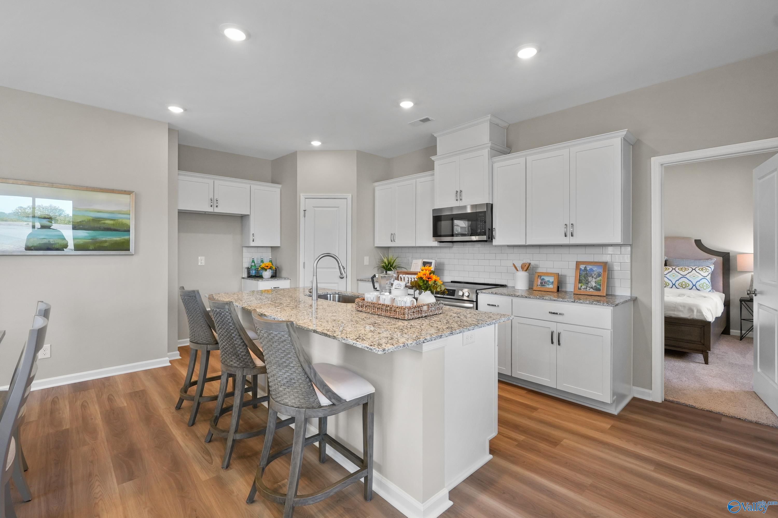 Modern kitchen with white cabinets, granite island, stainless appliances, and bar stools in Evermore Homes The Malibu, Madison, Alabama