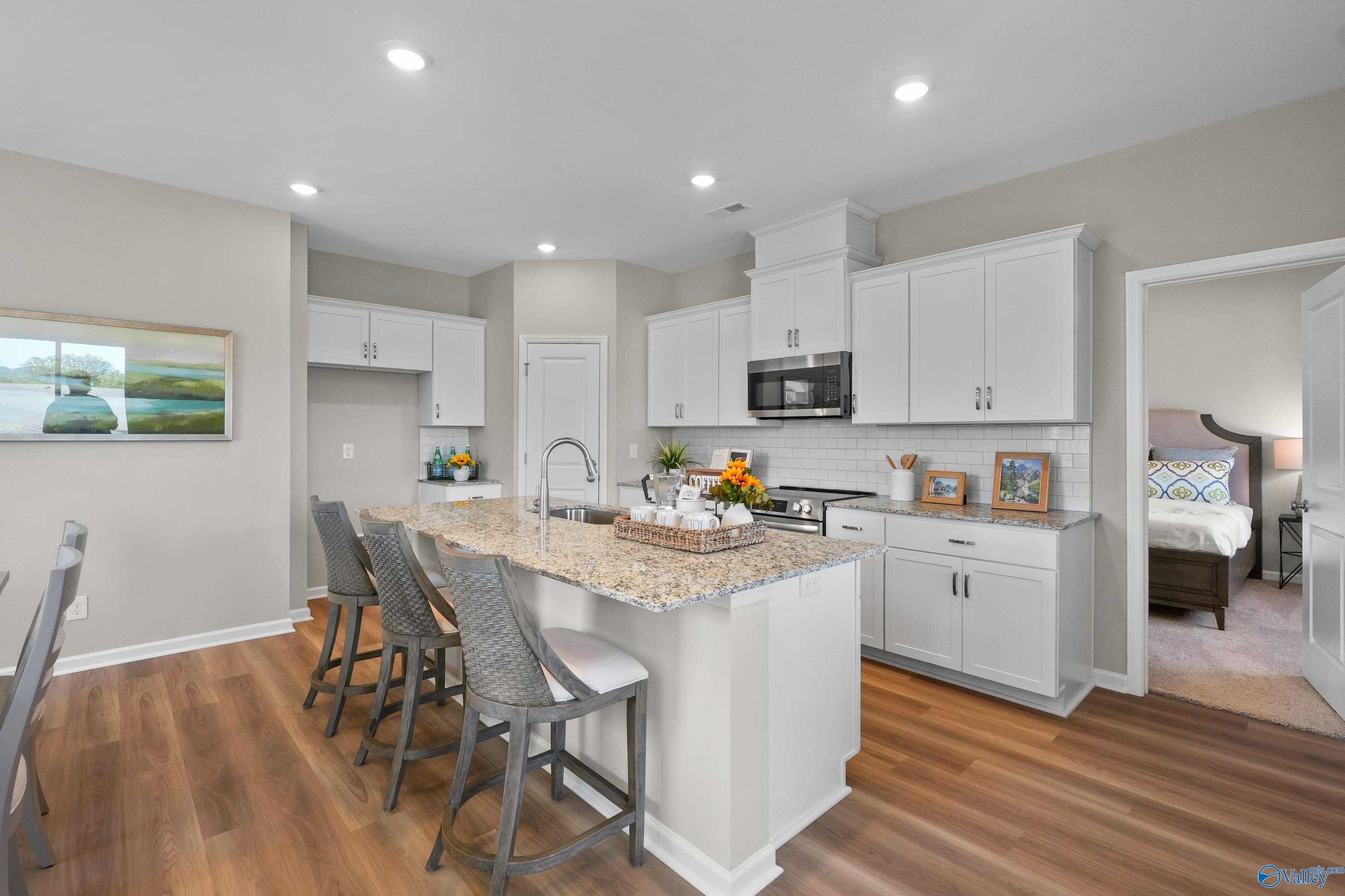 Modern kitchen with white cabinets, granite island, stainless appliances, and bar stools in Evermore Homes The Malibu, Madison, Alabama
