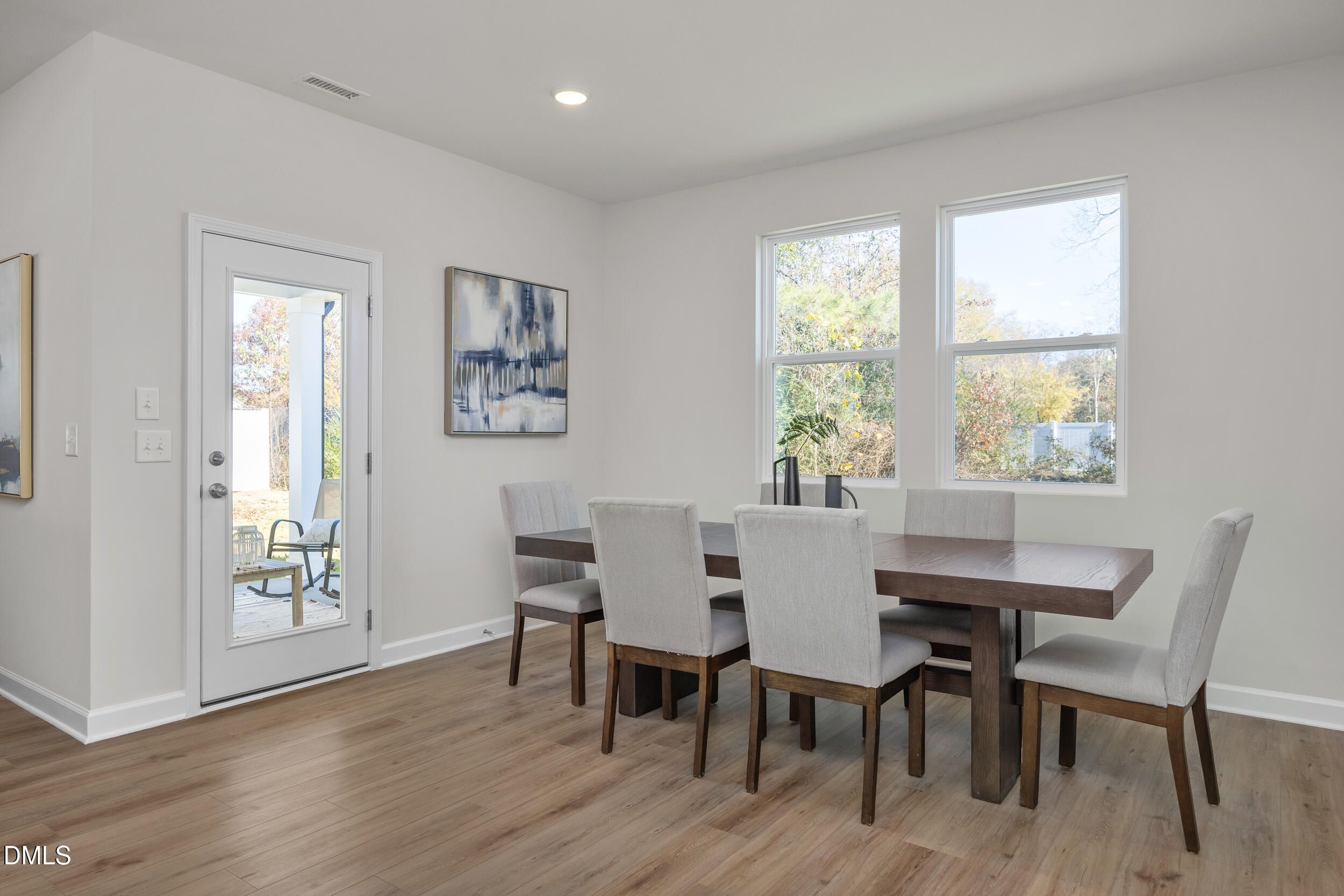 Bright dining room with rectangular wooden table, gray upholstered chairs, abstract art, large windows, and patio door in The Preston C home, Lillington, NC