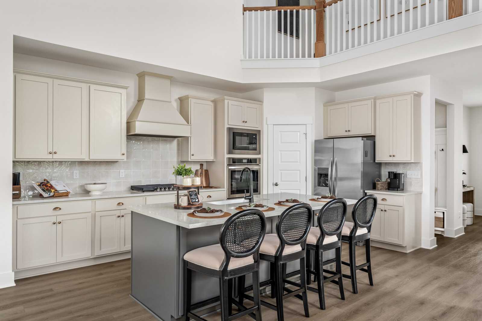 Open-concept kitchen at Woods Crossing in Gallatin TN with white cabinets, gray island, bar stools, and loft balcony