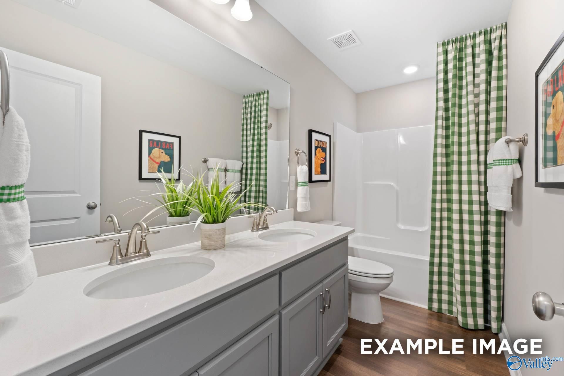 Modern bathroom with double vanity, gray cabinets, green gingham shower curtain, tub, and artwork in Davidson Homes The Stella, Madison, Alabama