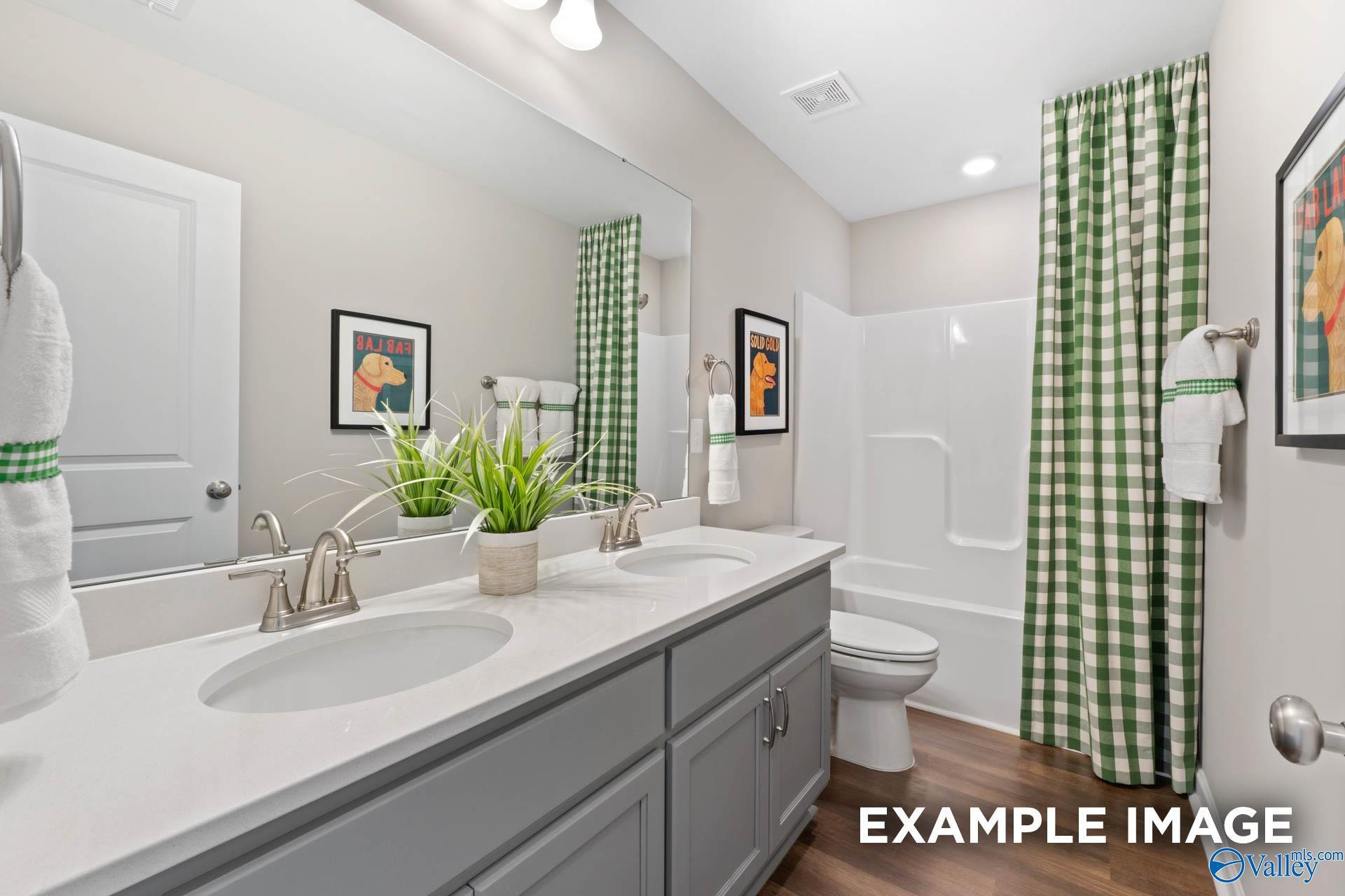 Modern bathroom with double vanity, gray cabinets, green gingham shower curtain, tub, and artwork in Davidson Homes The Stella, Madison, Alabama