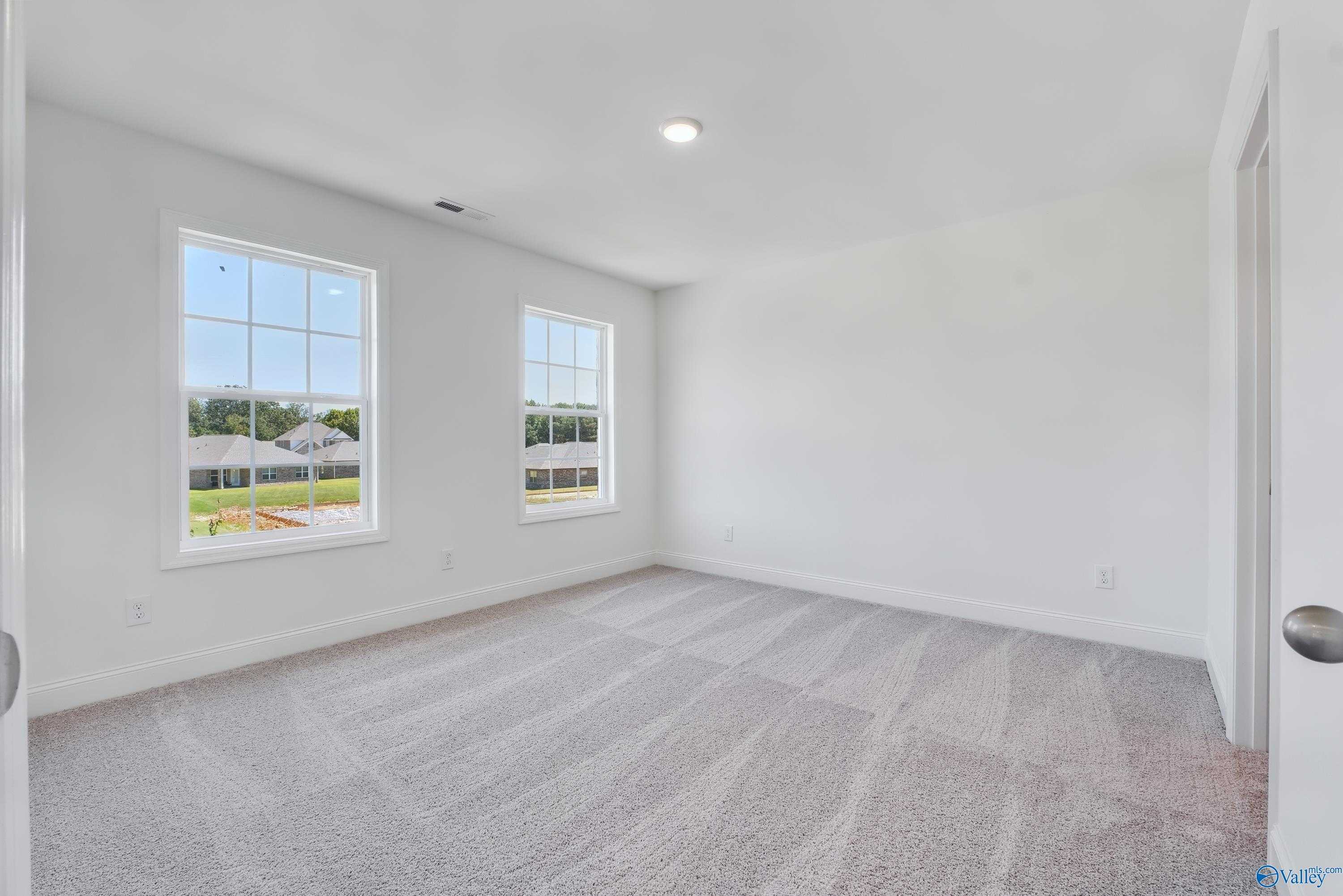 Spacious secondary bedroom with large windows overlooking lush greenery, neutral walls, and carpeted floors in The Shelby A, Arab, Alabama