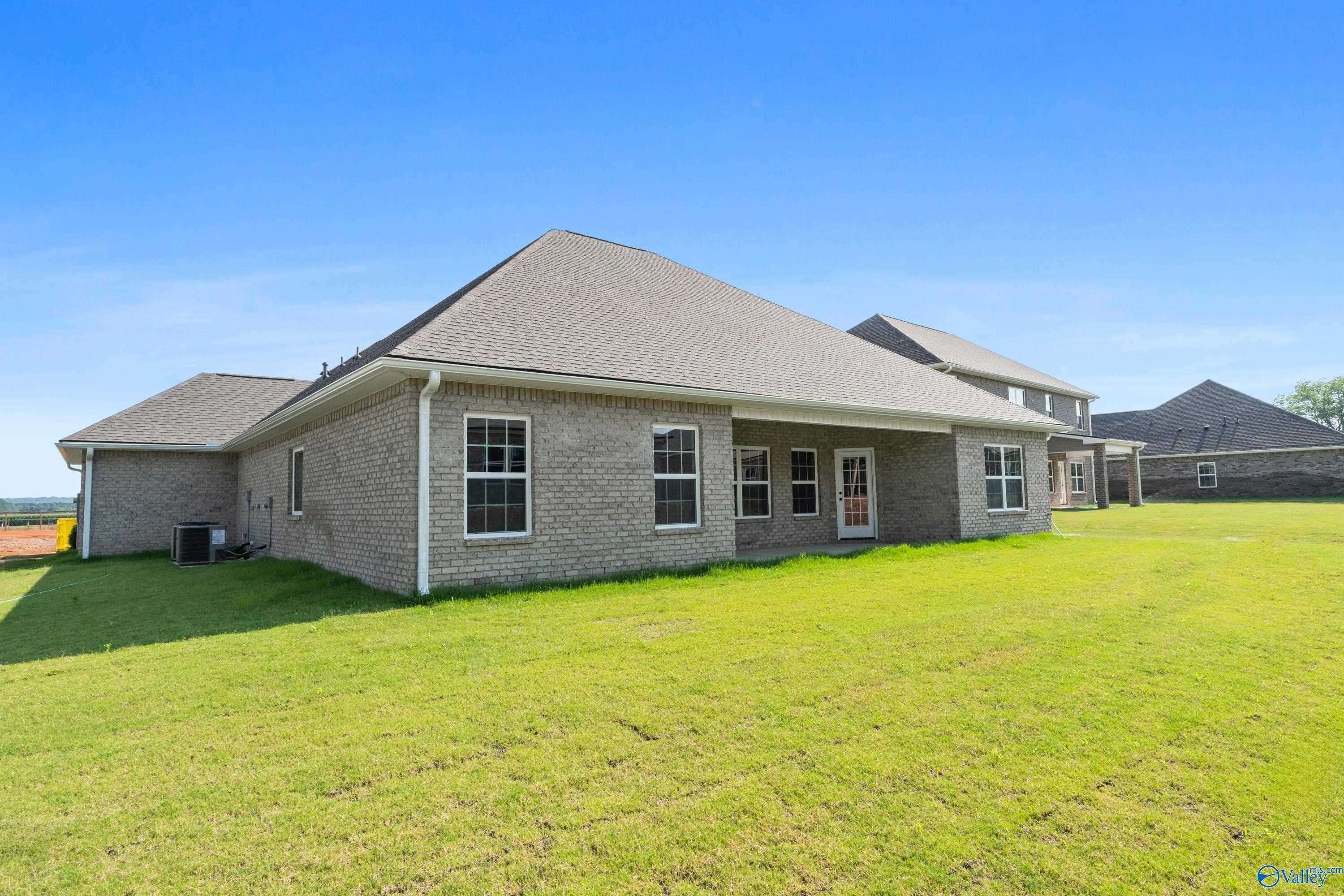 Brick one-story home rear with covered patio, large windows, and lush green backyard in Kendall Farms, Toney, Alabama