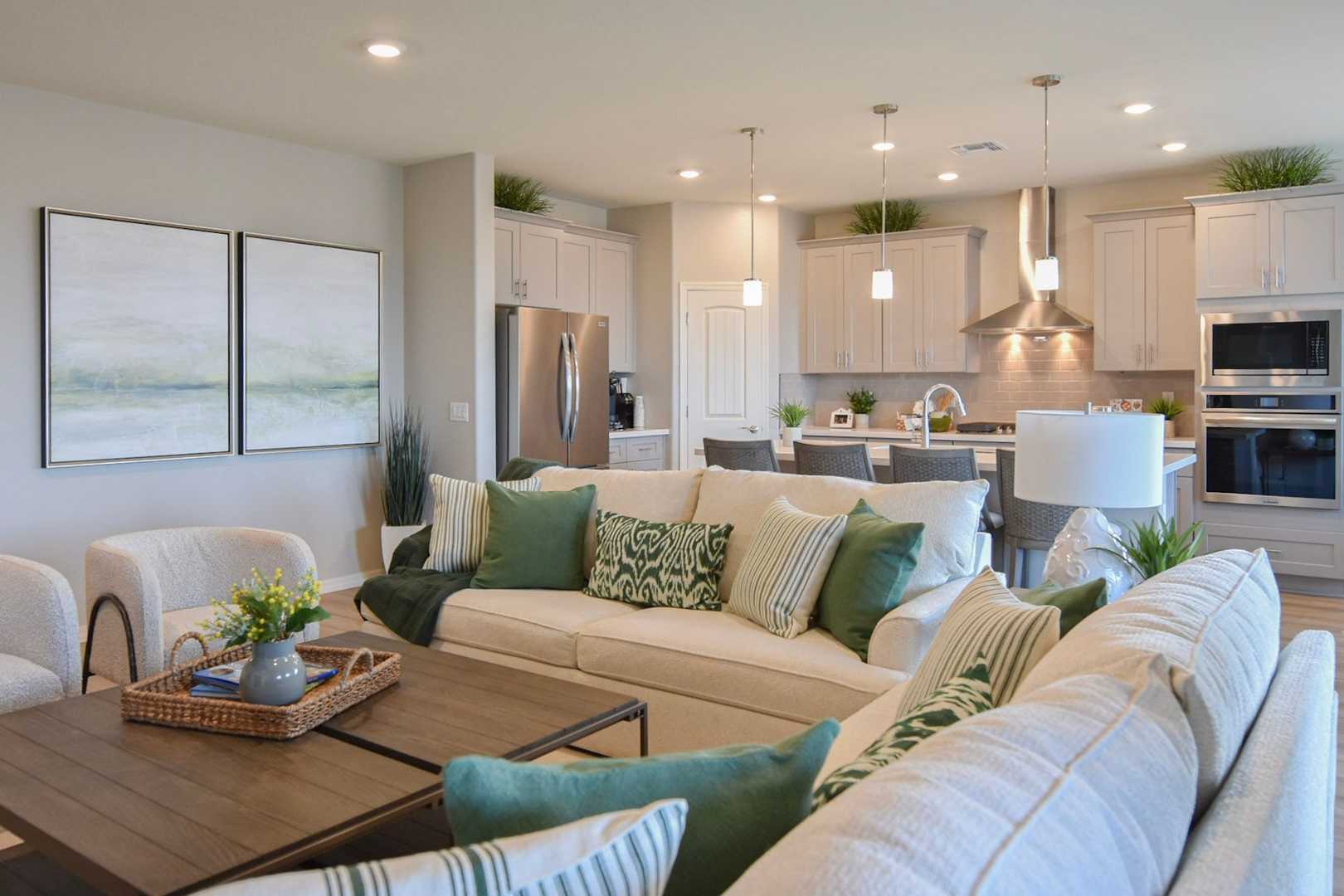 Open-concept living room and kitchen in The Harmony by Davidson Homes featuring white cabinets, stainless appliances, and plush neutral sofa