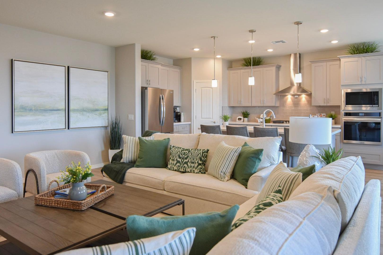 Open-concept living and kitchen in The Harmony B showcasing white shaker cabinets, L-shaped sofa with green pillows, and modern island
