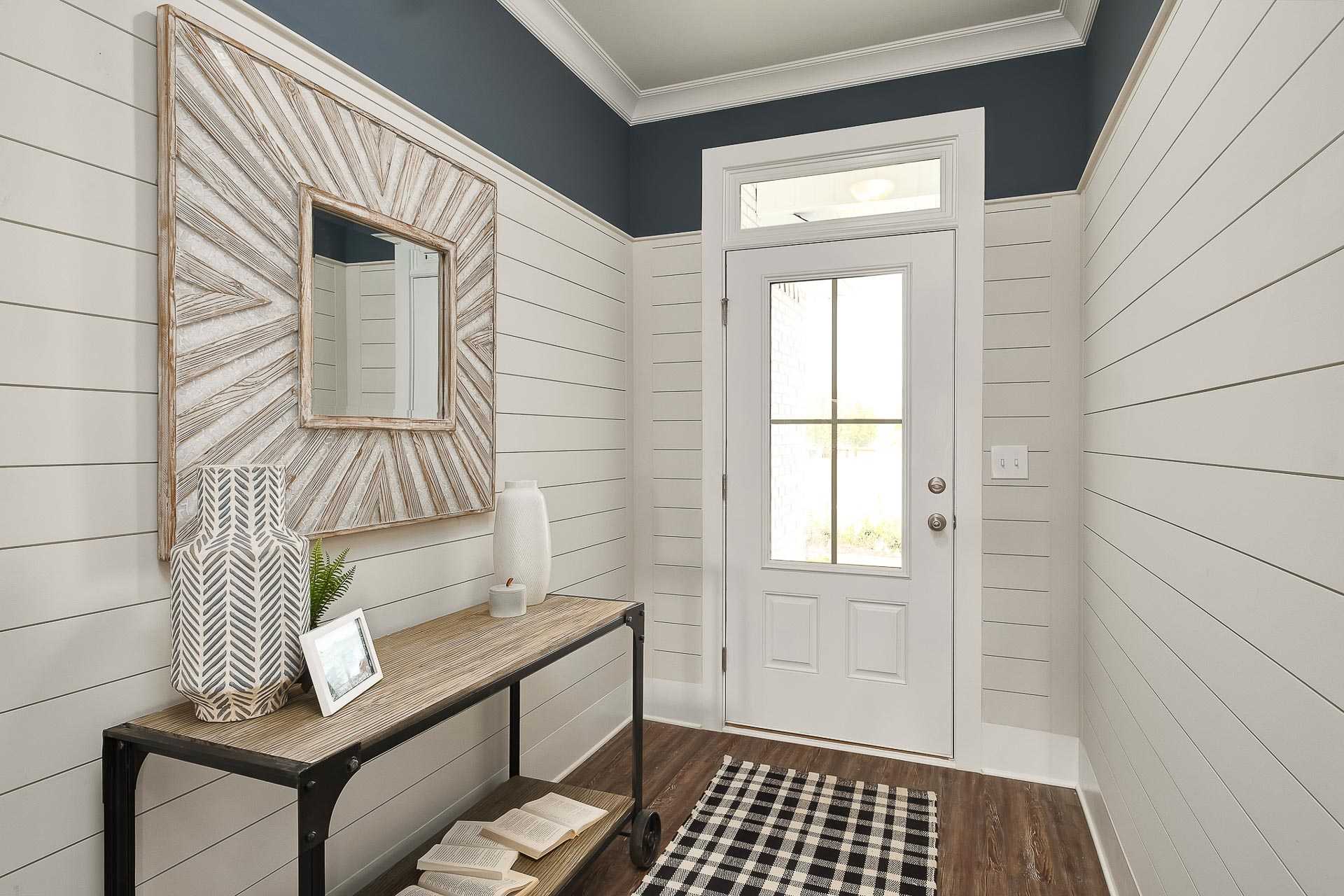 Spacious entryway in The Everett C home featuring white shiplap walls, navy trim, framed mirror, console table, and glass door