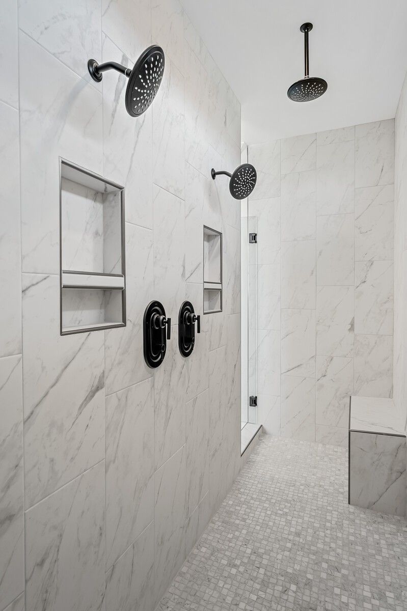 Luxurious white marble walk-in shower with rain showerheads, niches, and bench in The Alston A master bath, Murfreesboro, Tennessee
