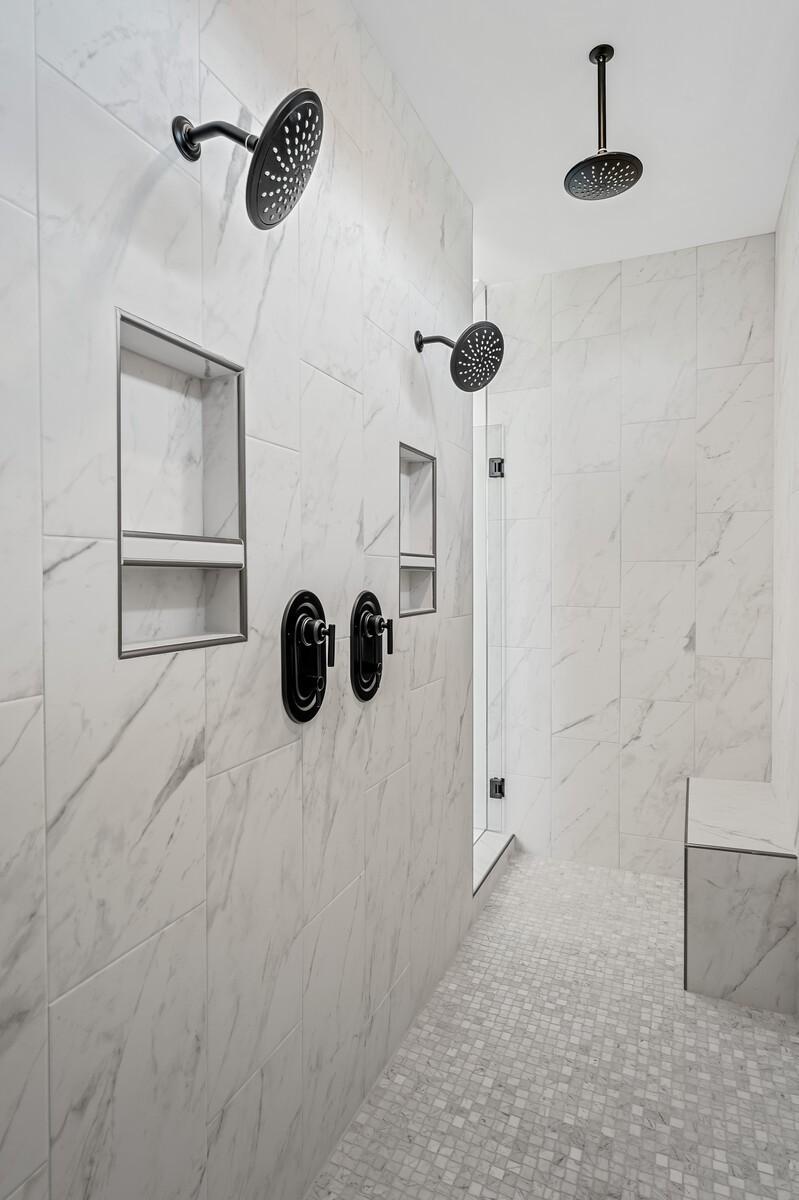 Luxurious white marble walk-in shower with rain showerheads, niches, and bench in The Alston A master bath, Murfreesboro, Tennessee