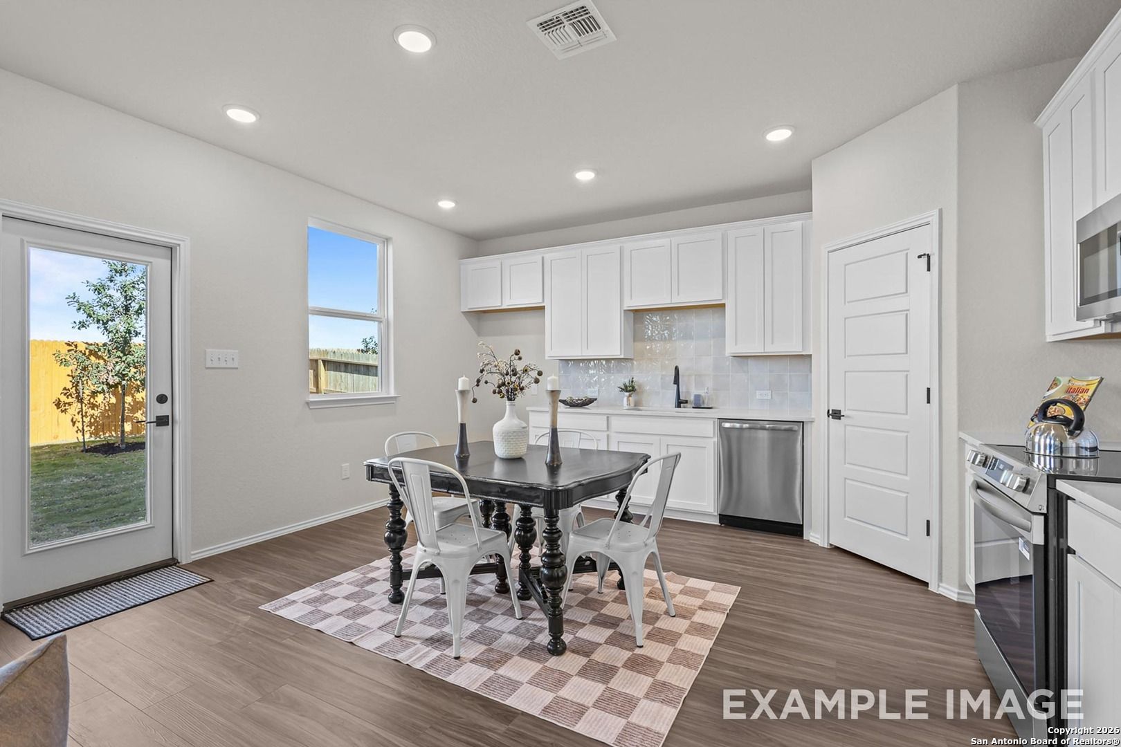 Bright dining nook with wooden farmhouse table, white chairs, checkered rug, and French doors to backyard in Davidson Homes Trinity B, San Antonio