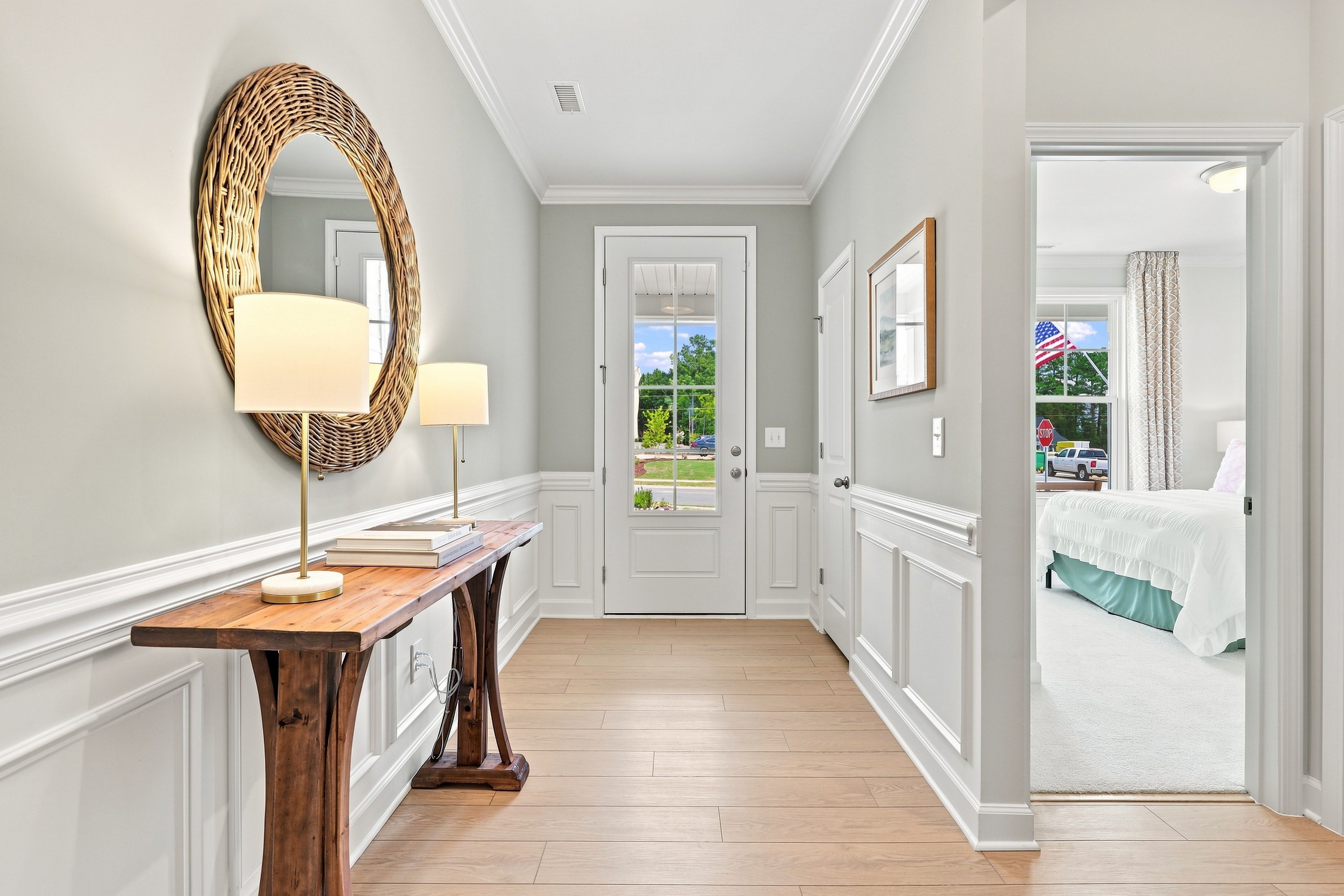 Bright foyer in The Daphne by Davidson Homes featuring wainscoting, wood console table, and view of the master suite.