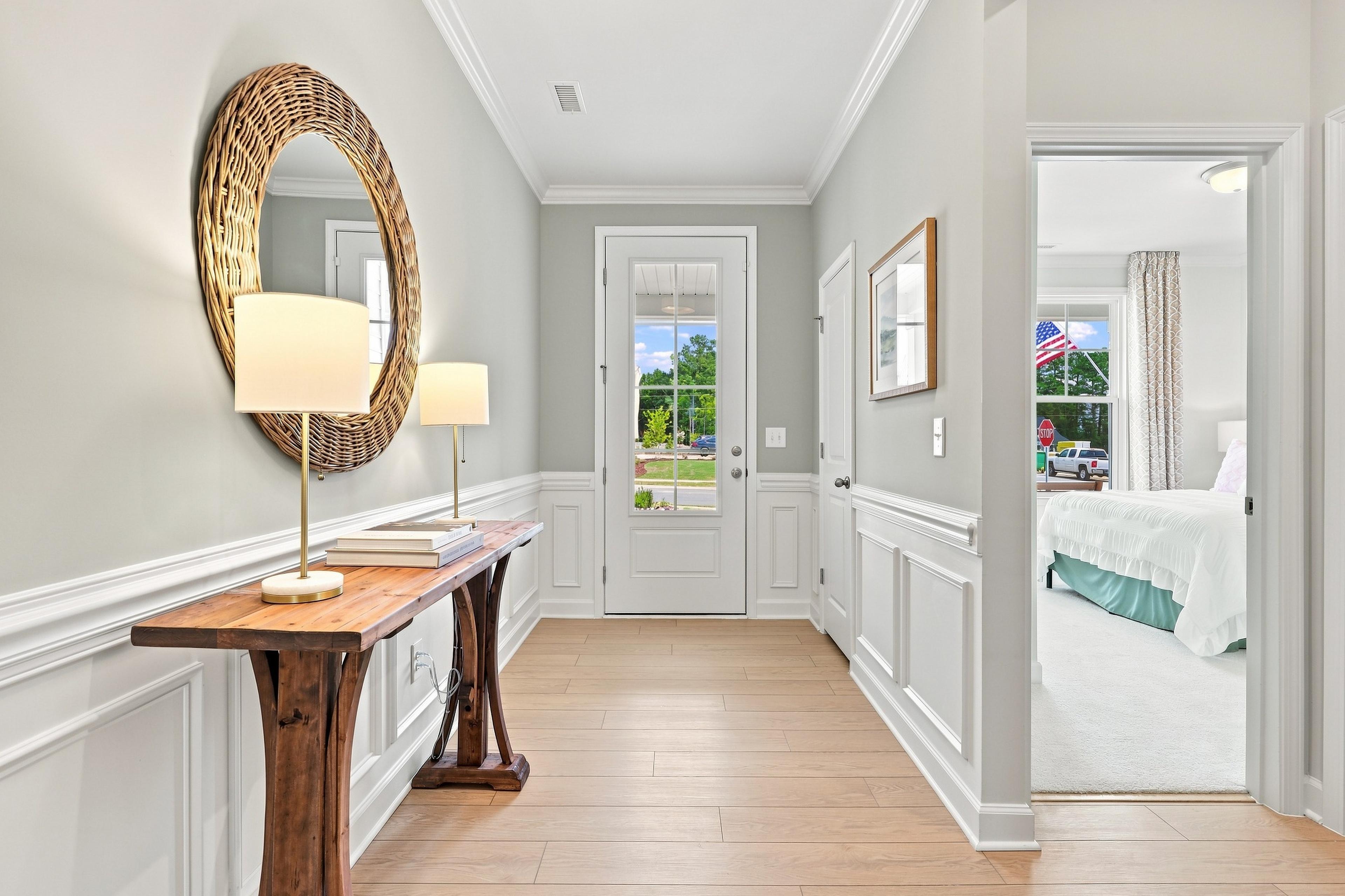 Bright foyer in The Daphne by Davidson Homes featuring wainscoting, wood console table, and view of the master suite.