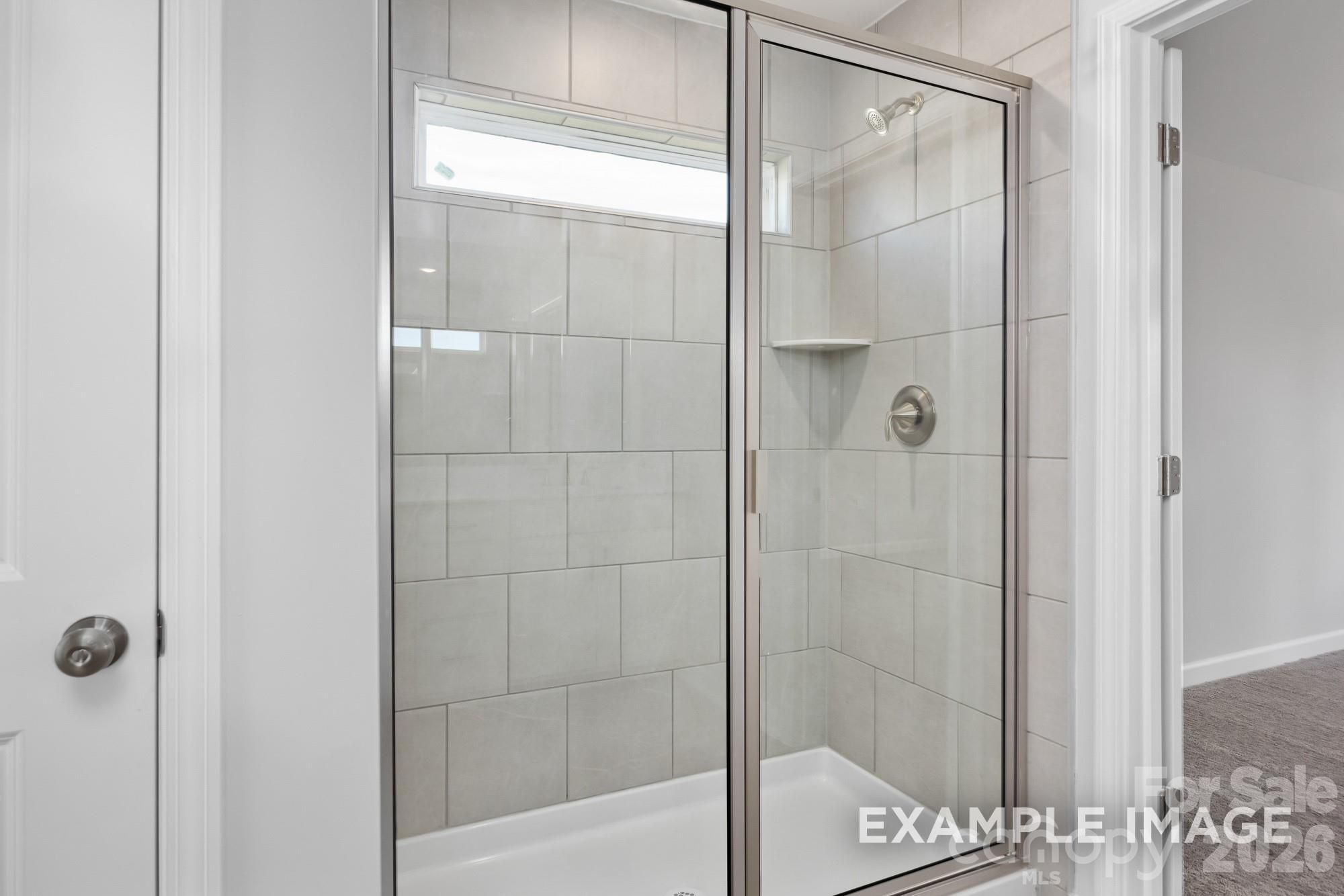 Tiled walk-in shower with glass door and brushed nickel fixtures in bathroom of Davidson Homes Willow B, Mooresville NC