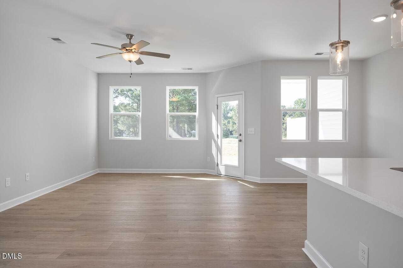 Bright open living room with hardwood floors, large windows, ceiling fan, and white kitchen island in Davidson Homes The Graham, Fuquay-Varina, NC
