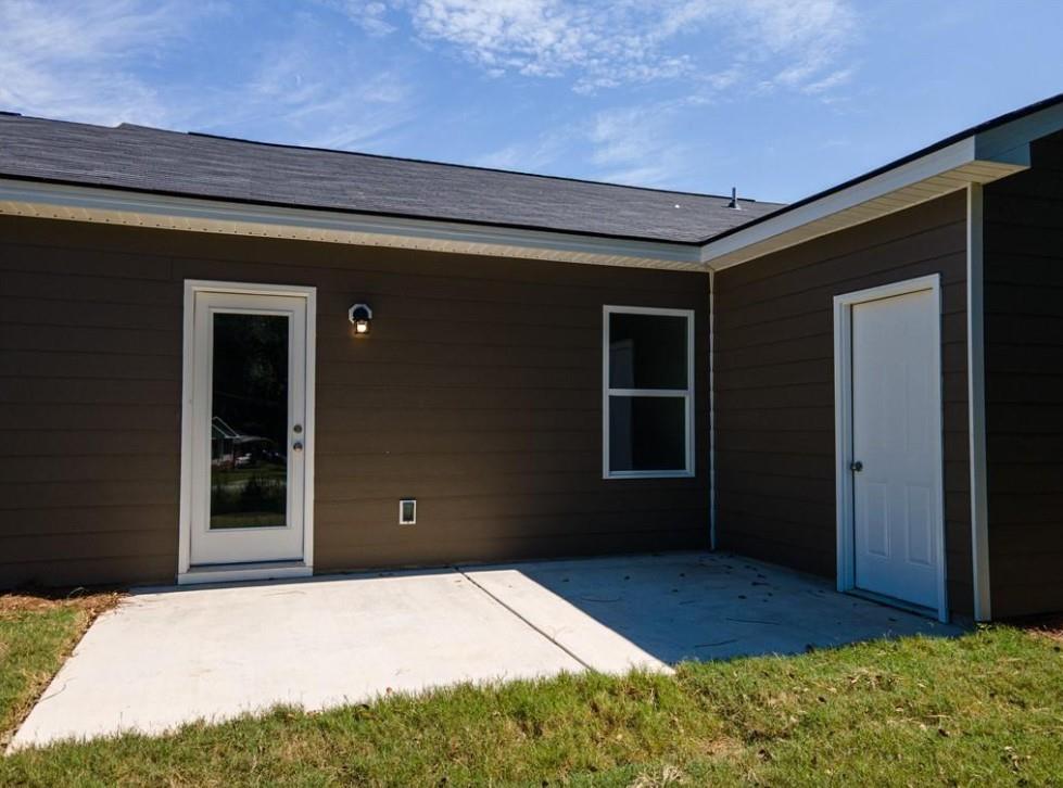 Back exterior of Davidson Homes The Washington with covered patio, glass door, and lush yard in Summer Vineyard, Phenix City, Alabama