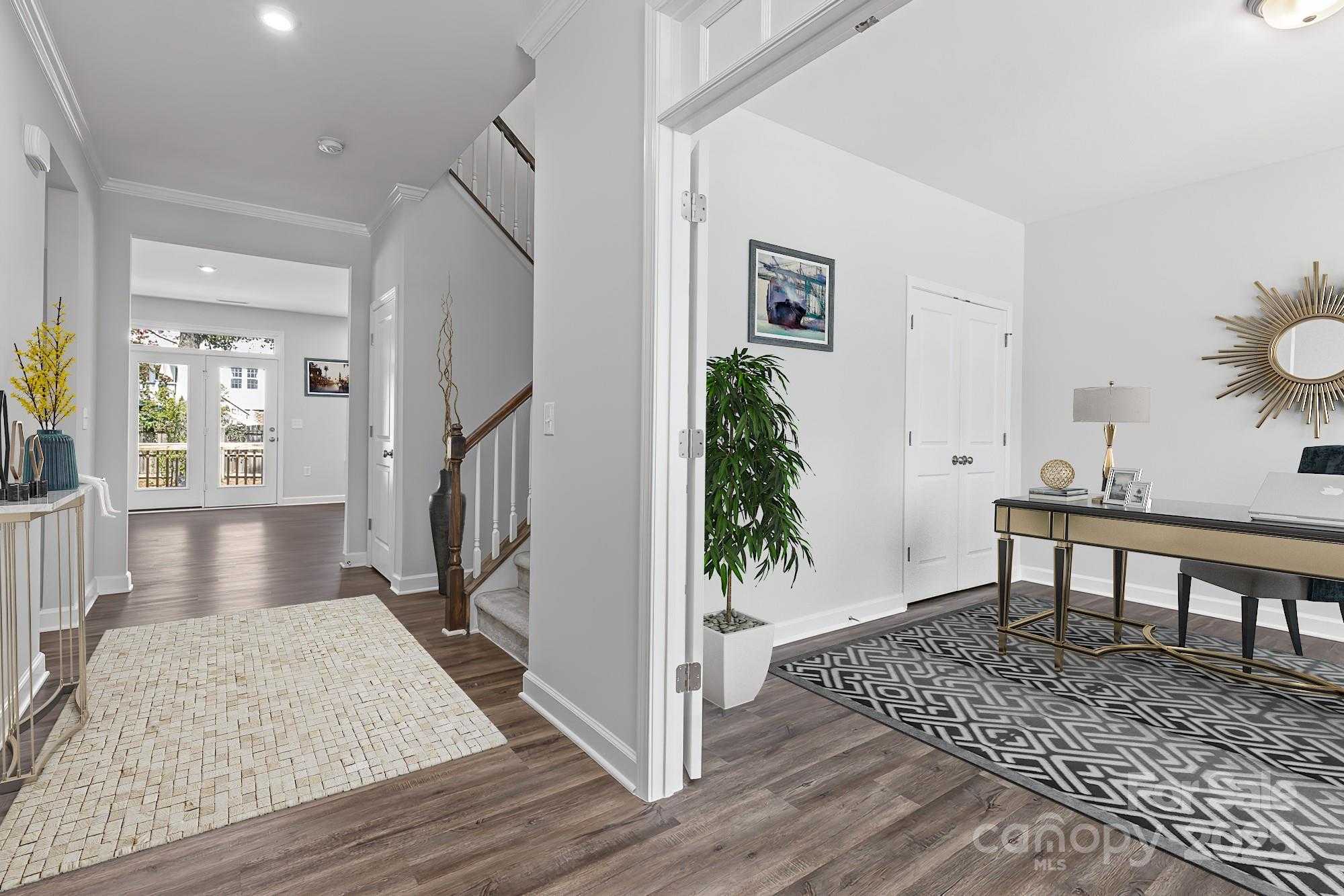 Elegant foyer hallway with oak staircase, potted plants, and adjacent modern home office desk in Davidson Homes The Hemlock A, Belmont, NC