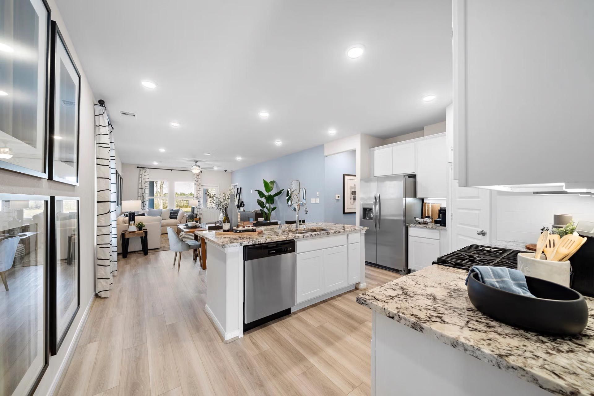 Spacious open-concept kitchen at Saddle Creek Ranch in Cibolo Texas with white cabinets granite island hardwood floors and living area