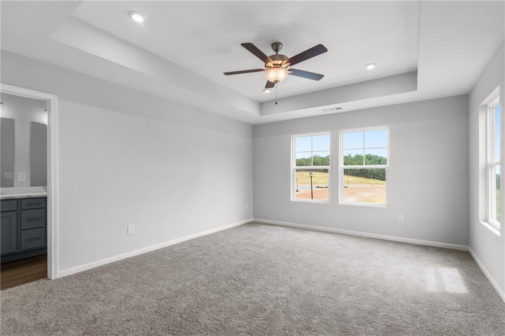 Spacious gray bedroom with tray ceiling, ceiling fan, and scenic windows in Davidson Homes The Monroe B, Emerson, Georgia