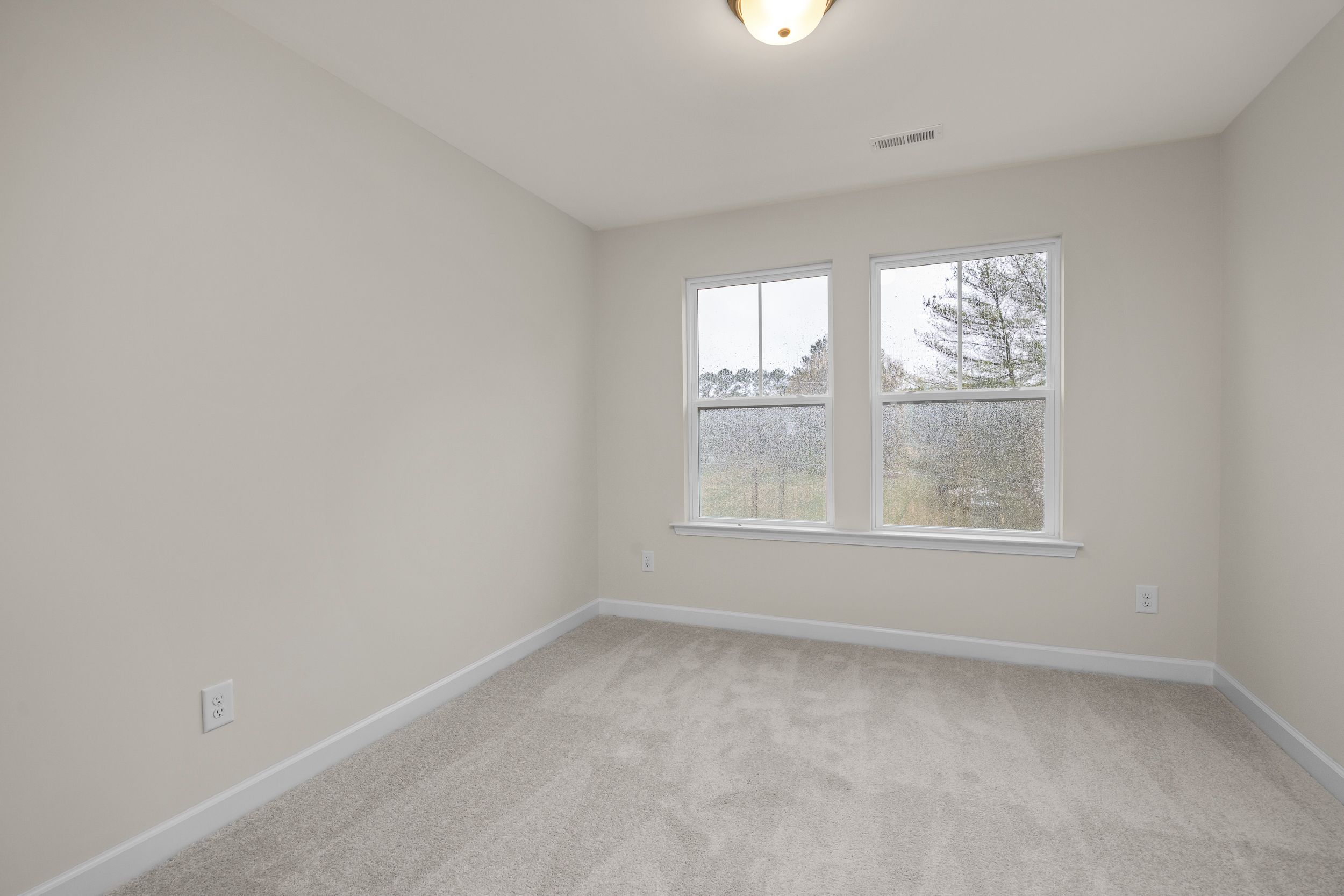 Bright bedroom with large windows overlooking woods at Forestville Yard Townhomes in Knightdale NC featuring beige carpet and neutral walls