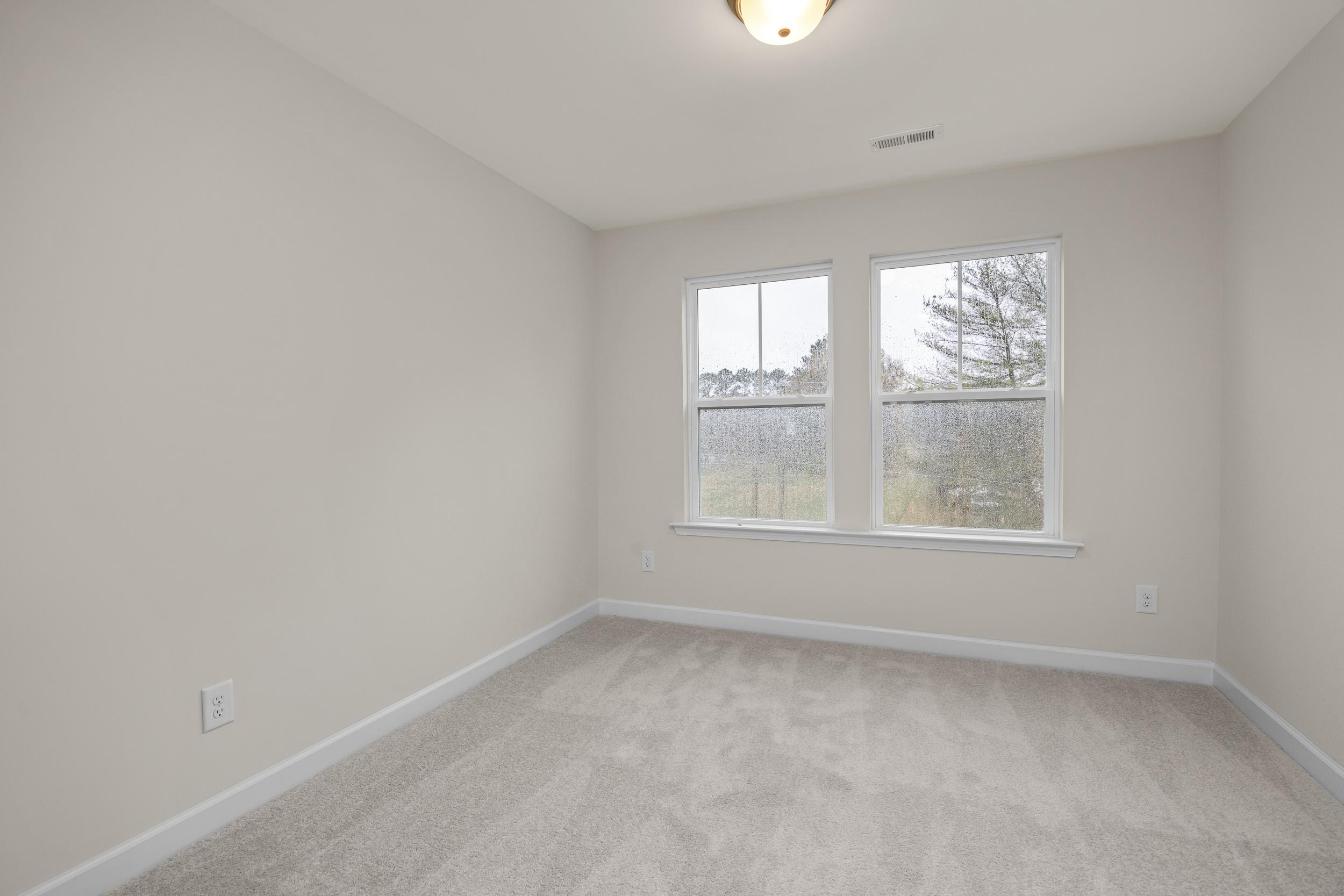 Bright bedroom with large windows overlooking woods at Forestville Yard Townhomes in Knightdale NC featuring beige carpet and neutral walls