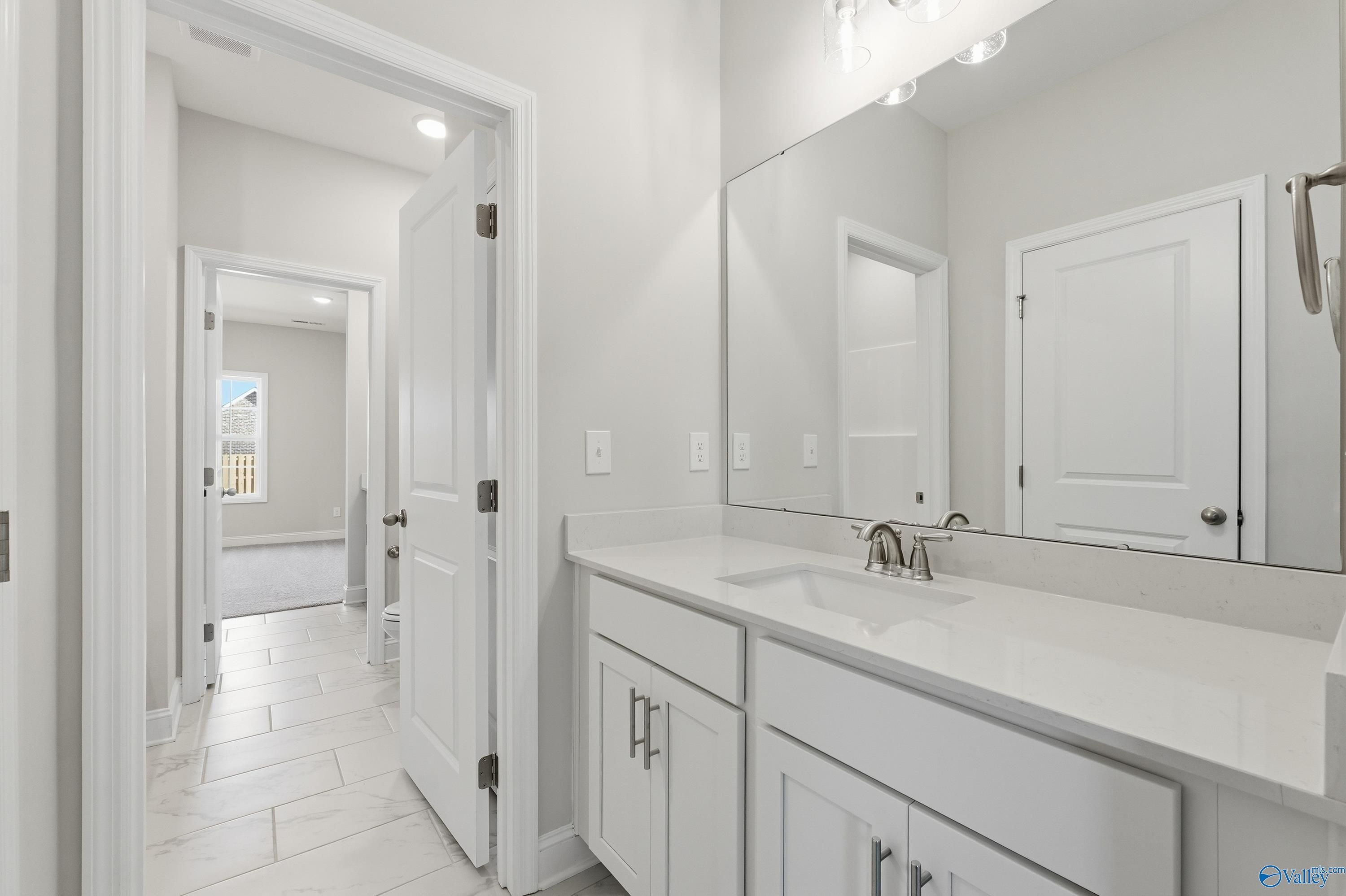 Bright white double vanity bathroom with large mirror, sink, and open hallway in Davidson Homes The Finleigh, Harvest, Alabama