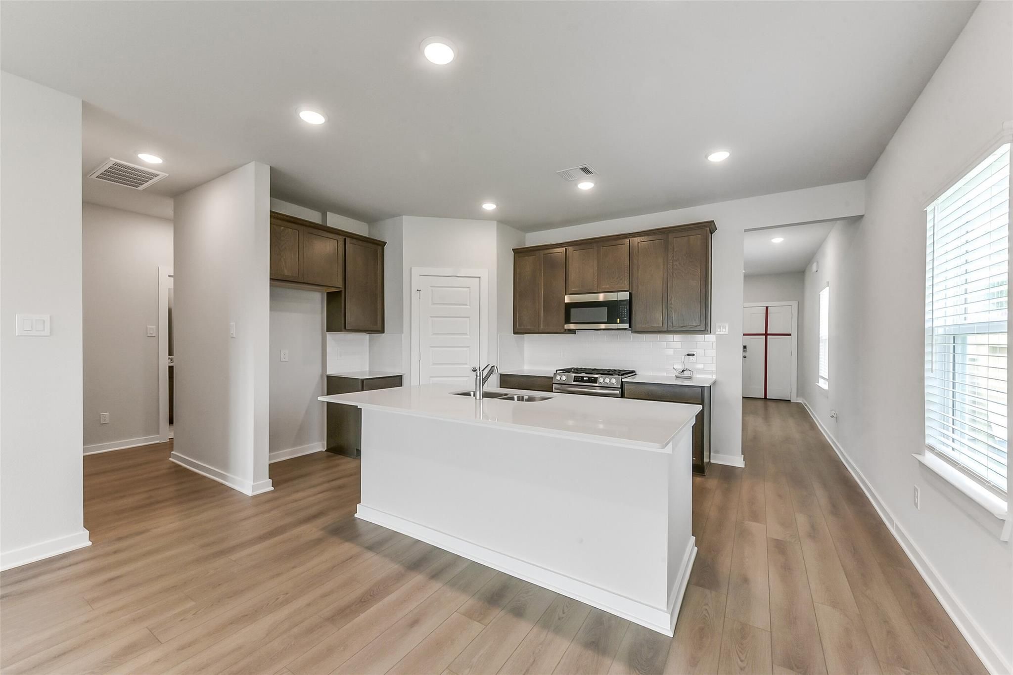 Open-concept kitchen with white quartz island, brown shaker cabinets, stainless appliances in Sabine F floor plan, Dayton Texas