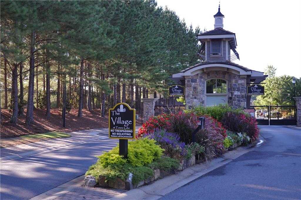 Elegant stone entrance gate to The Village at Towne Lake in Woodstock, Georgia, surrounded by pine trees and colorful flower beds