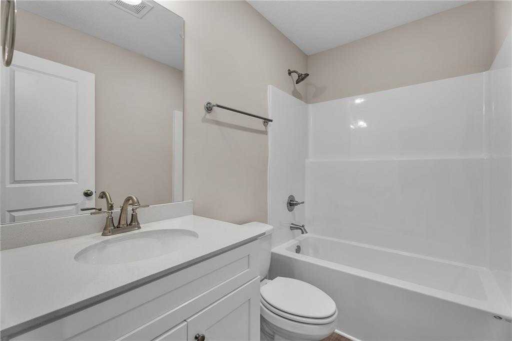 Bright guest bathroom with white vanity, tub, shower, and toilet in Davidson Homes The Bartlett, Phenix City, Alabama