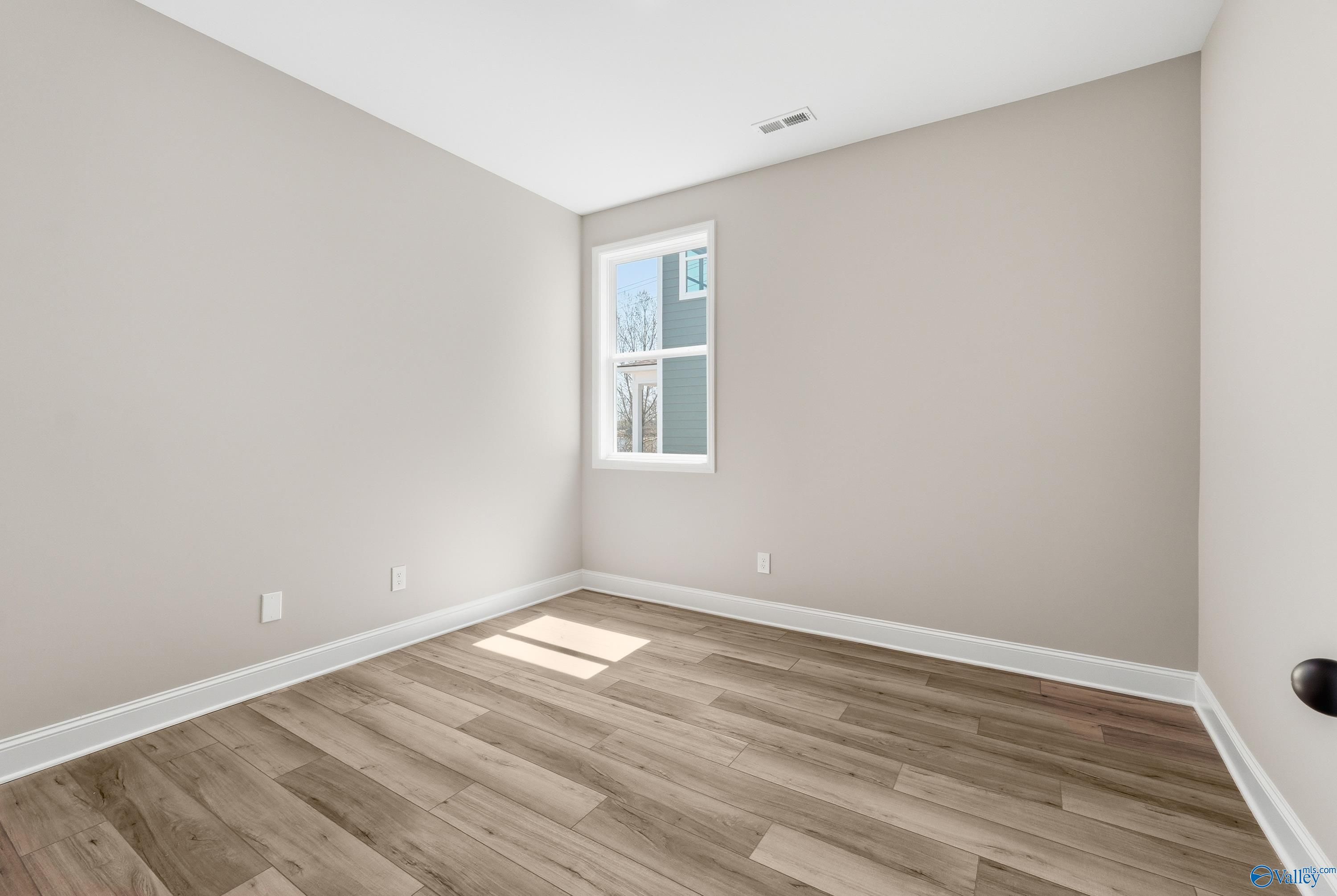 Empty secondary bedroom with light gray walls, large window with blinds, and hardwood floors in Davidson Homes The Laurel K, Cullman, Alabama
