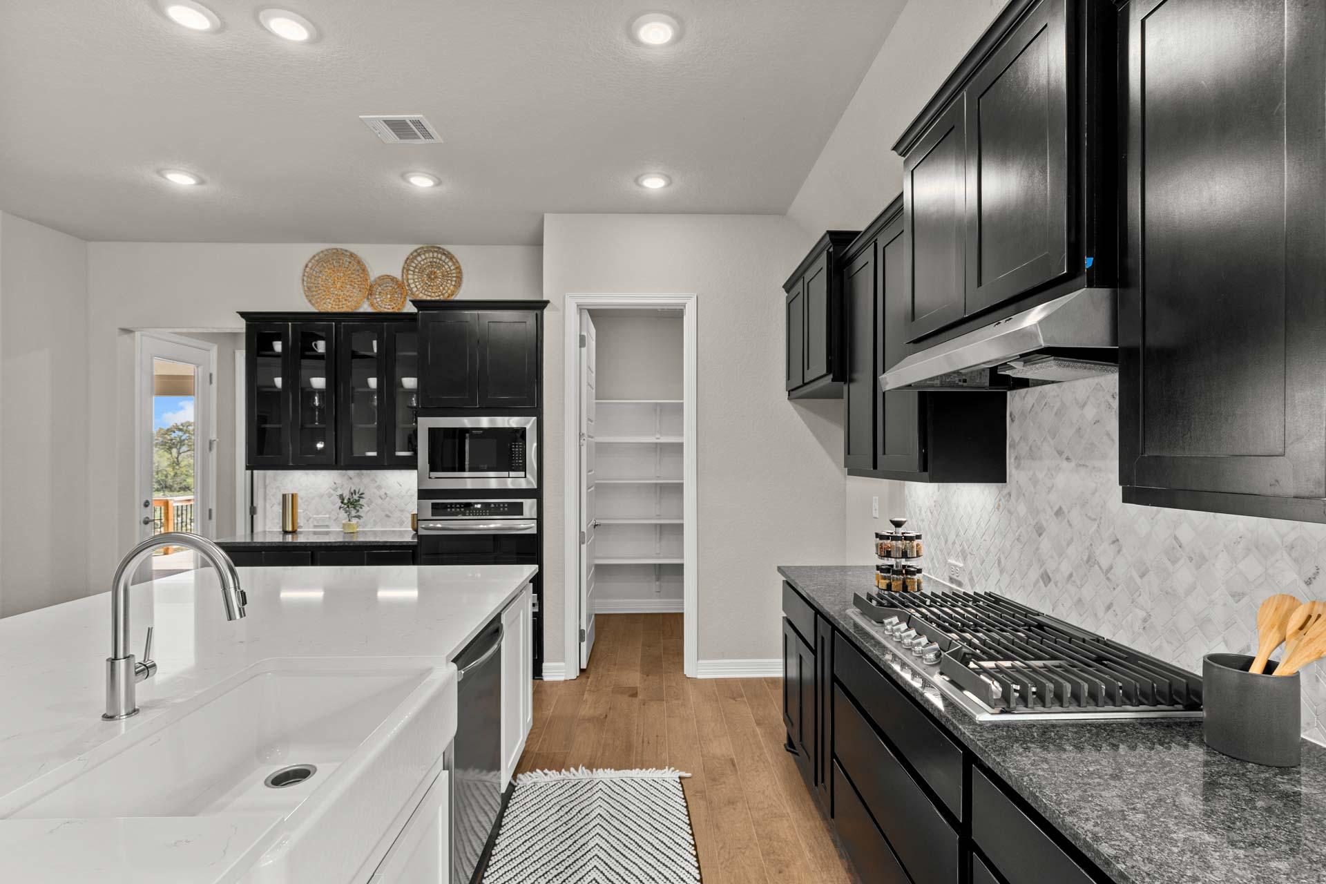 Modern kitchen in Potranco Oaks, Castroville Texas with black cabinets, white quartz island, gas range, and hardwood floors