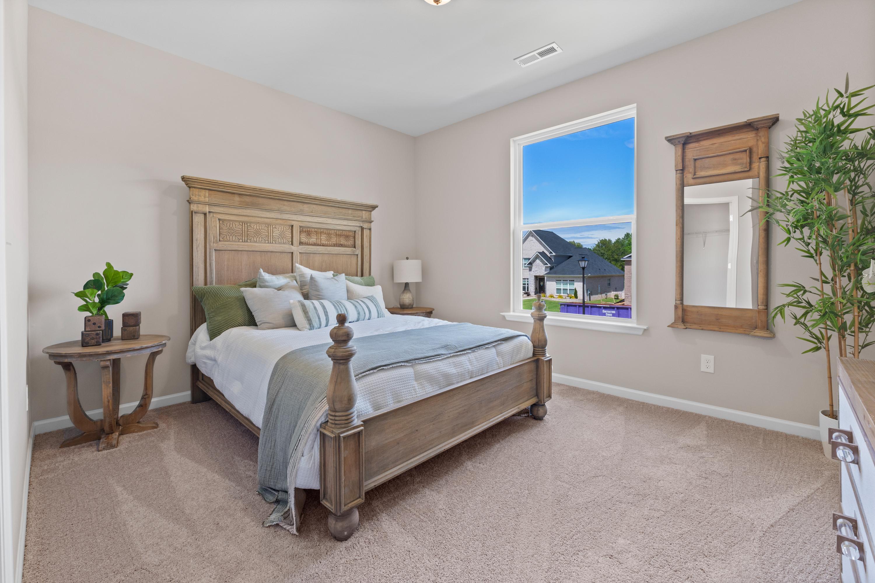 Cozy bedroom interior at Riverton Preserve in Huntsville AL with rustic wooden bed frame, neutral beige walls, and window overlooking neighborhood homes
