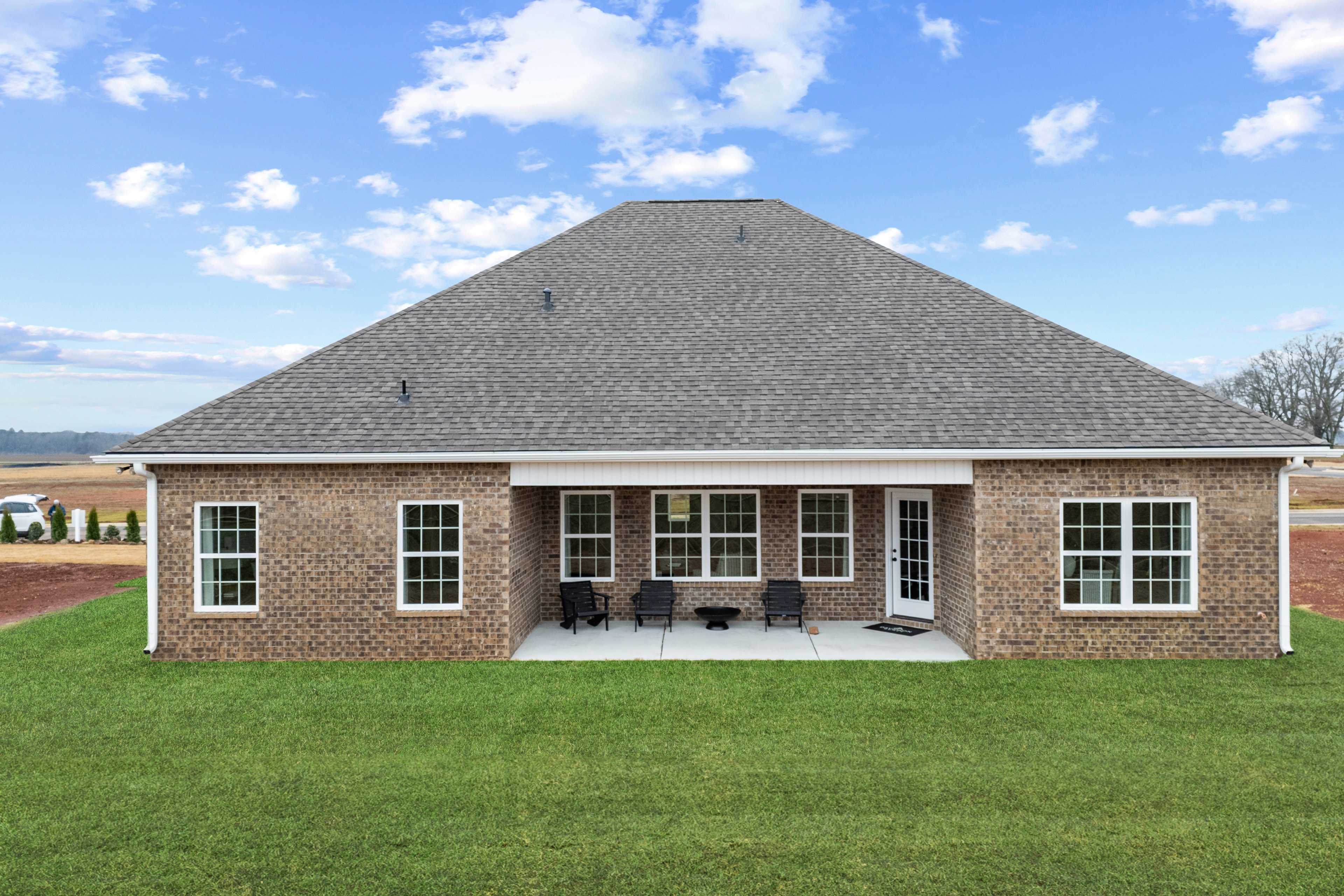 Rear view of single-story brick home at Kendall Farms in Toney, Alabama with covered patio, lounge chairs, and rural fields backdrop