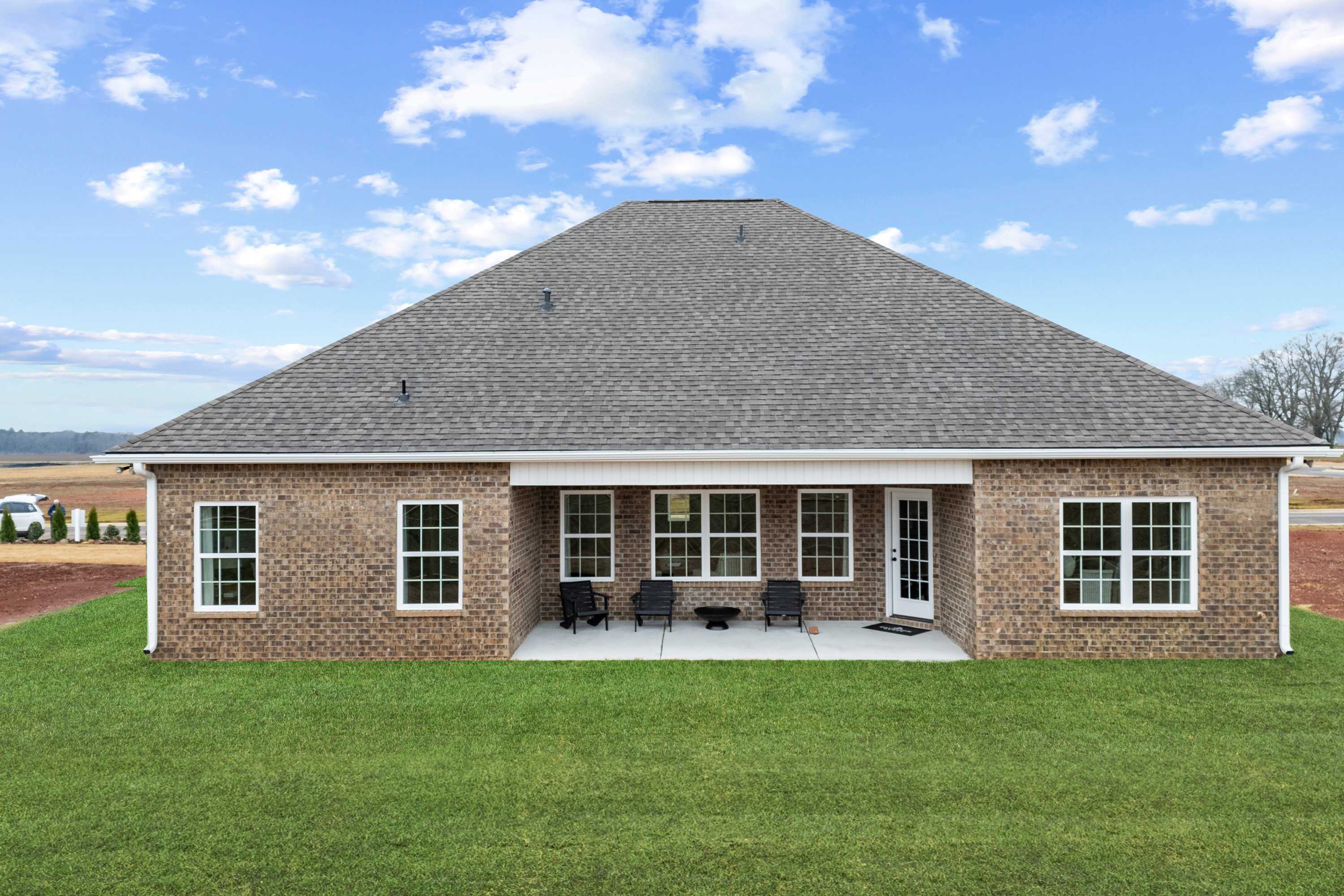 Rear view of single-story brick home at Kendall Farms in Toney, Alabama with covered patio, lounge chairs, and rural fields backdrop